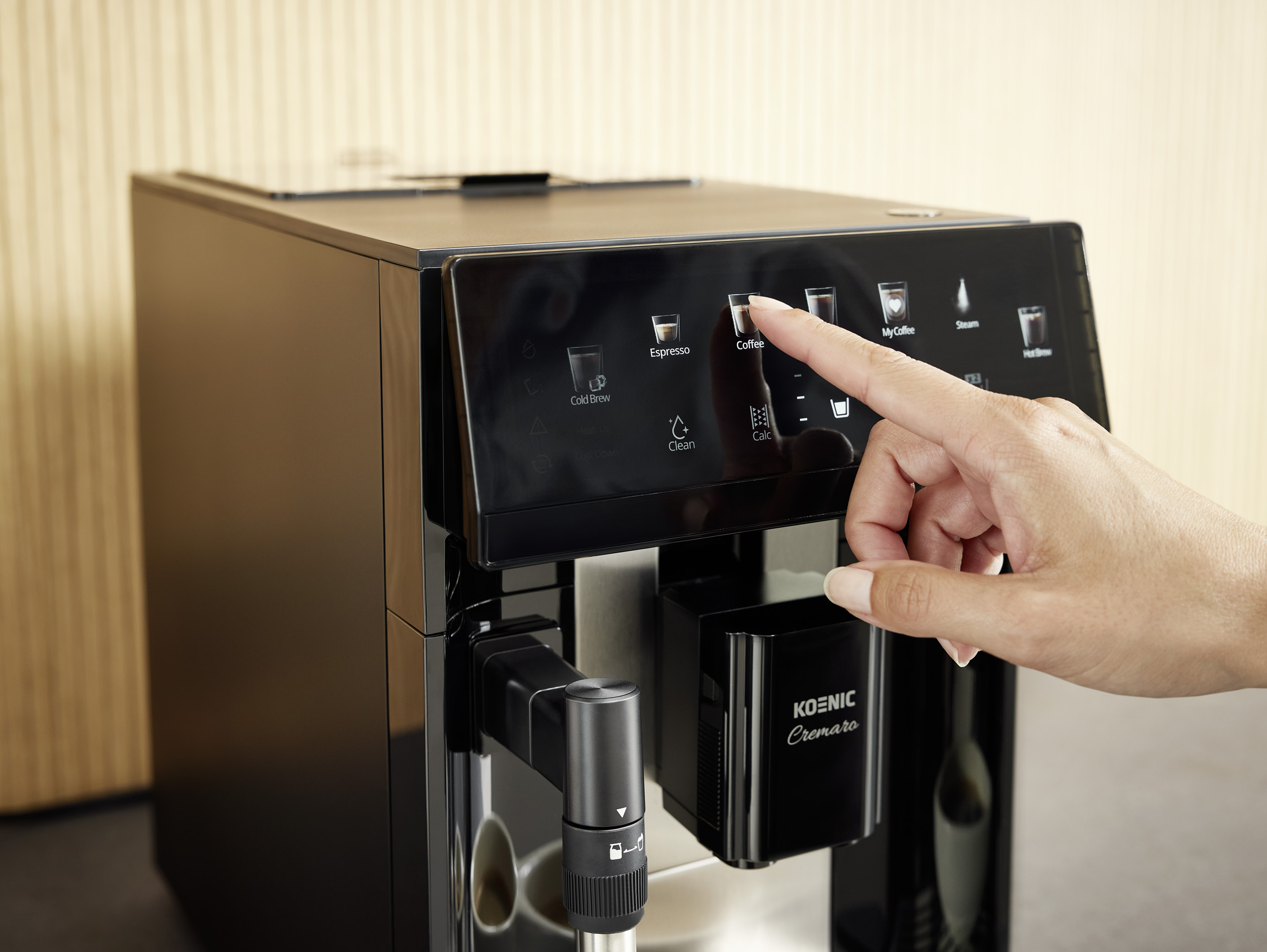 Eine Hand tippt auf das Touchdisplay eines schwarzen Koenic-Kaffeevollautomaten.