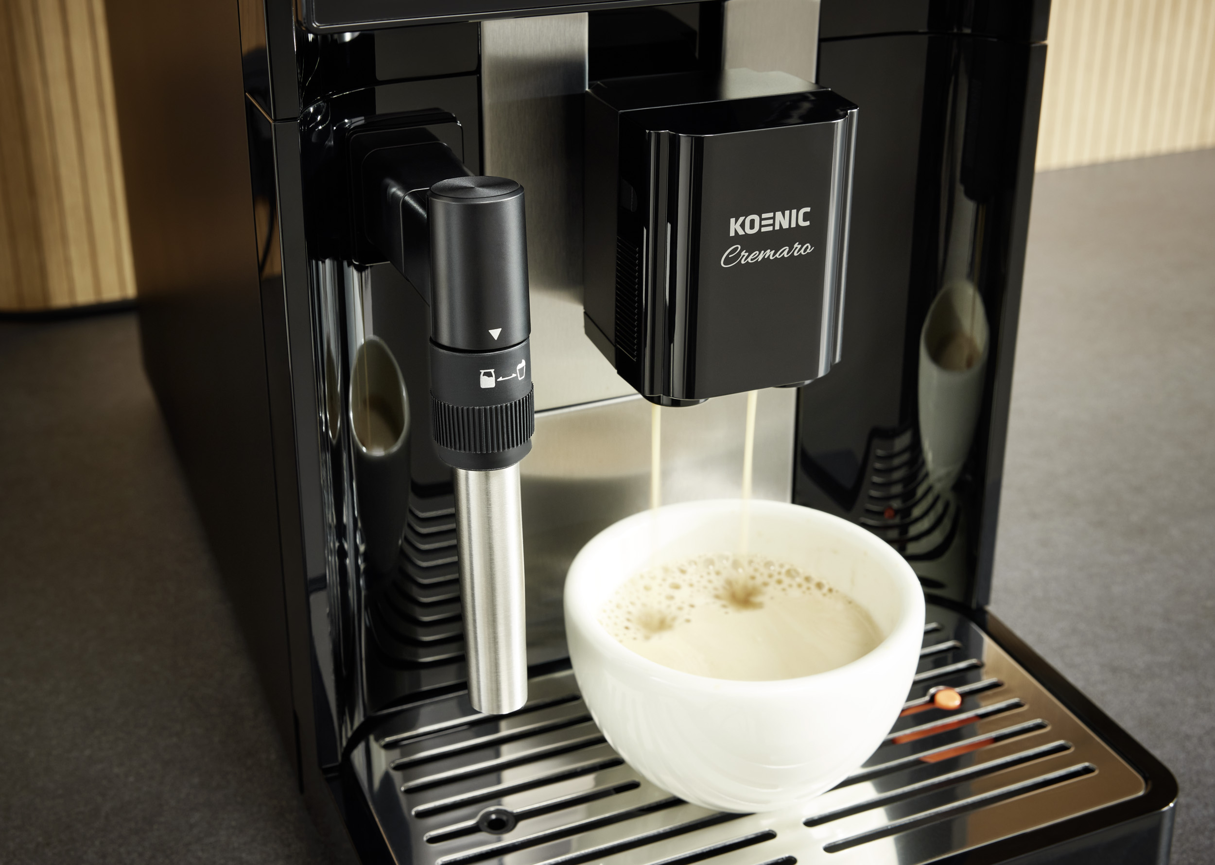 Eine schwarze Koenic Cremaro Kaffeemaschine brüht Kaffee in eine weiße Tasse auf einem Metalldrip.