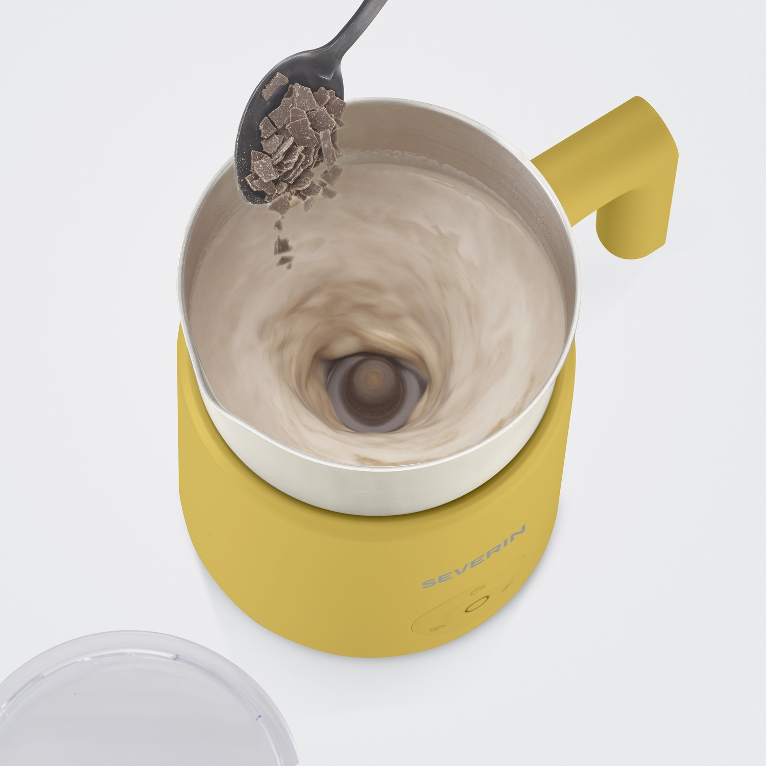 Pezzi di cioccolato vengono versati da un cucchiaio in un montalatte giallo con latte in vortice.