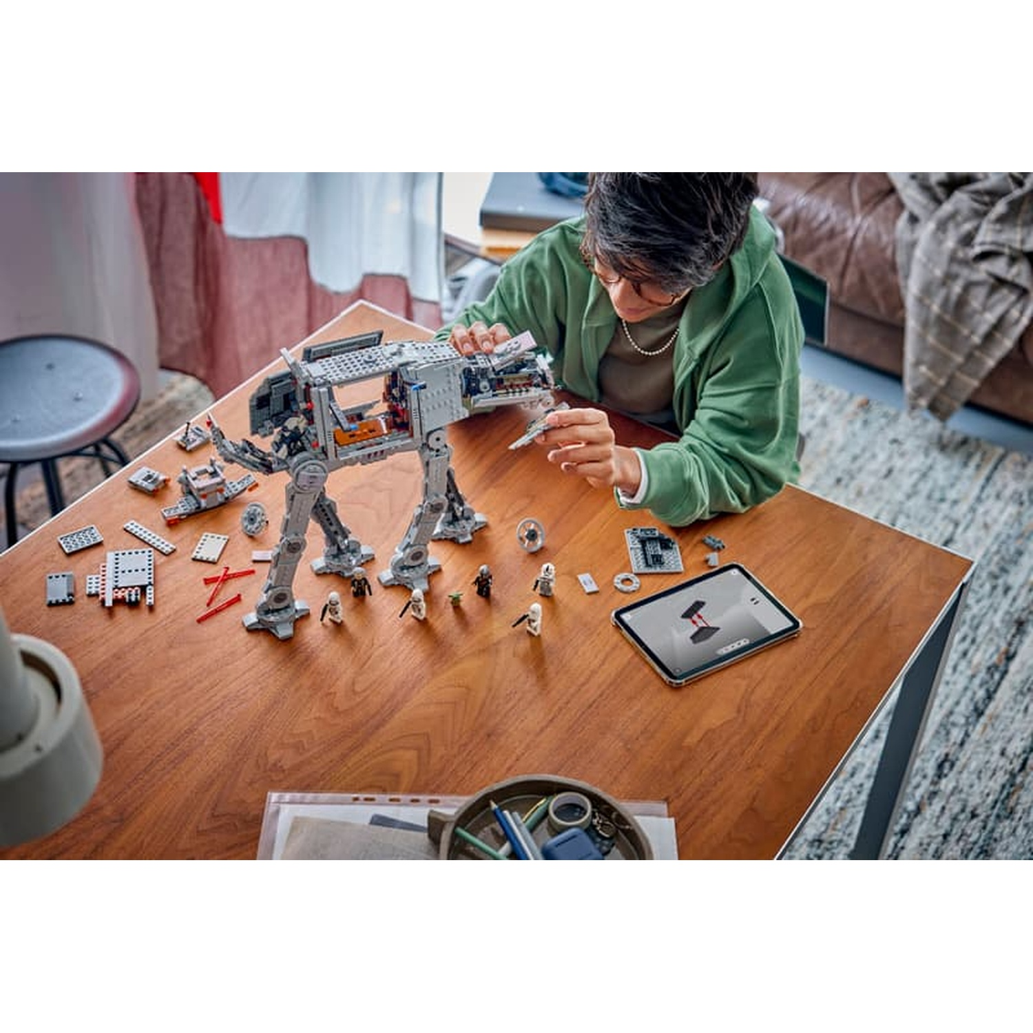 Una persona costruisce un modello Lego AT-AT su un tavolo di legno con un tablet.