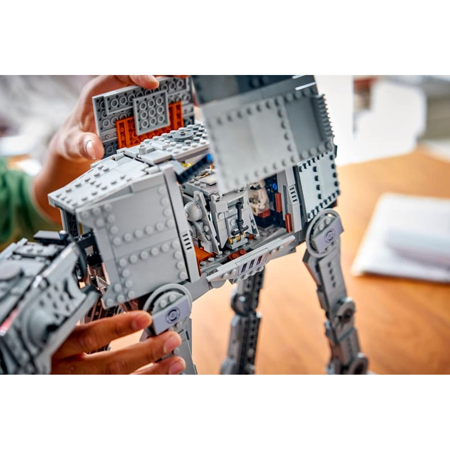 Mani che costruiscono e aprono un modello grigio LEGO Star Wars AT-ST Walker su un tavolo di legno.