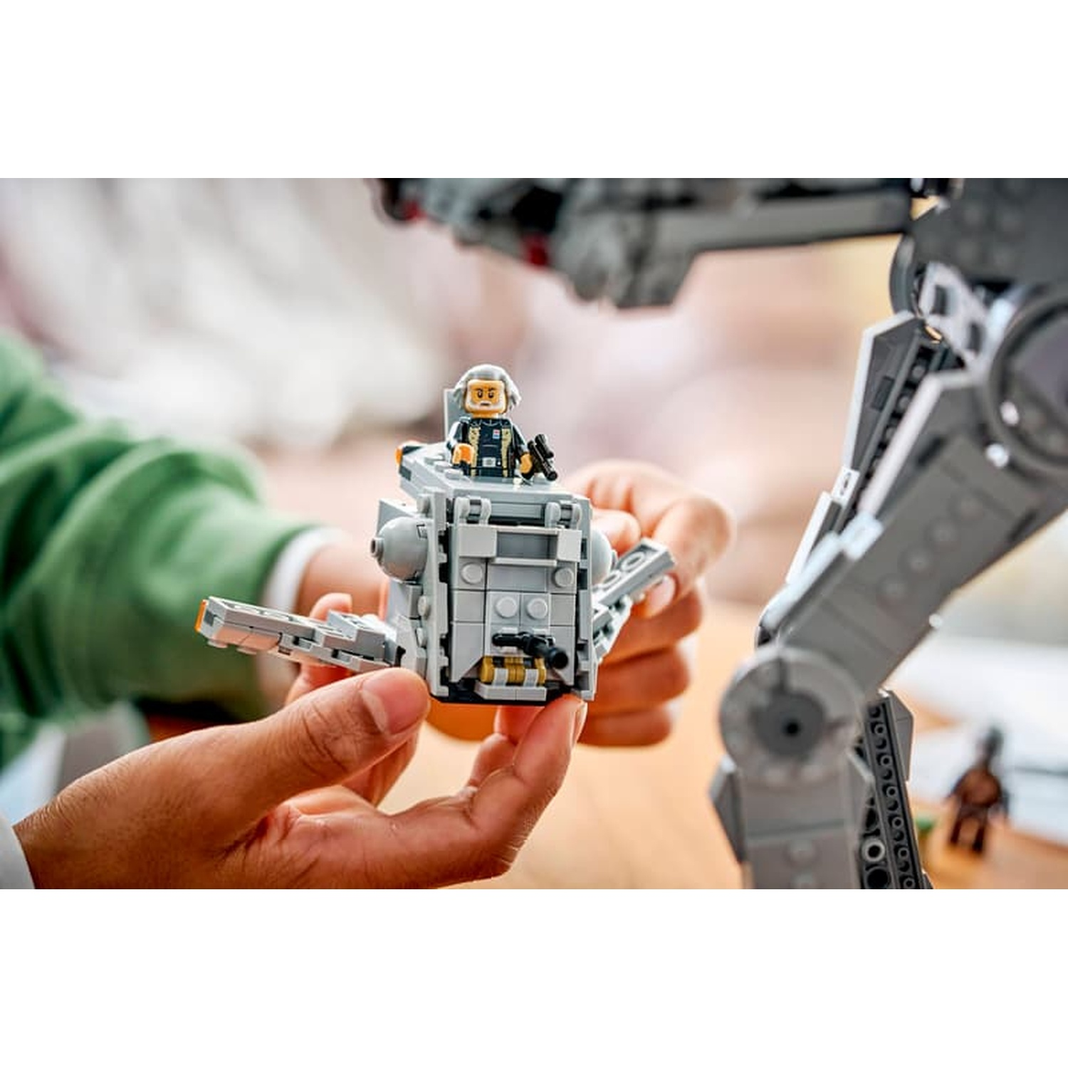 Persona che tiene una piccola astronave LEGO con minifigura, con un grande camminatore sullo sfondo.