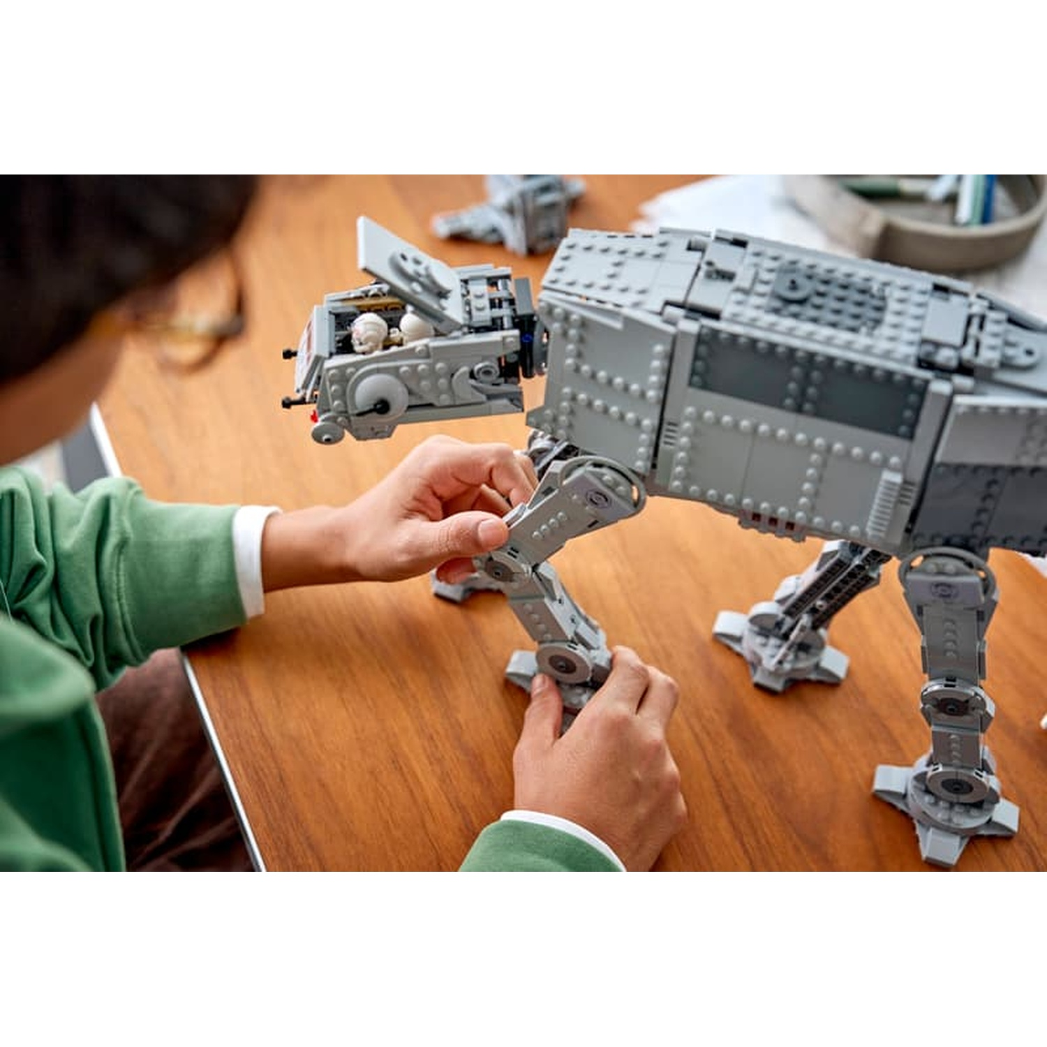 Un bambino costruisce un grande camminatore Lego grigio su un tavolo di legno.