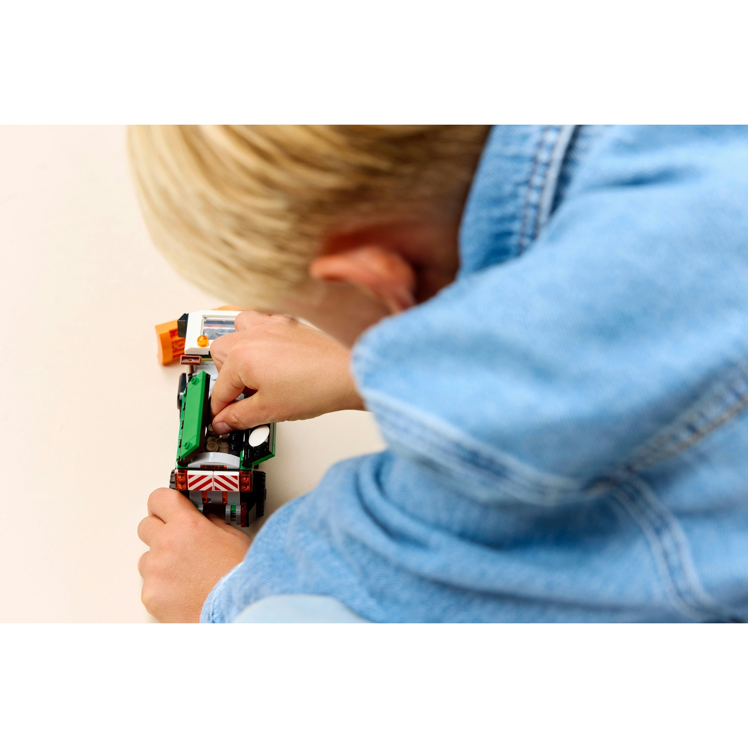 Un bambino biondo con una giacca di jeans blu gioca concentrato con un piccolo veicolo giocattolo su un tavolo.