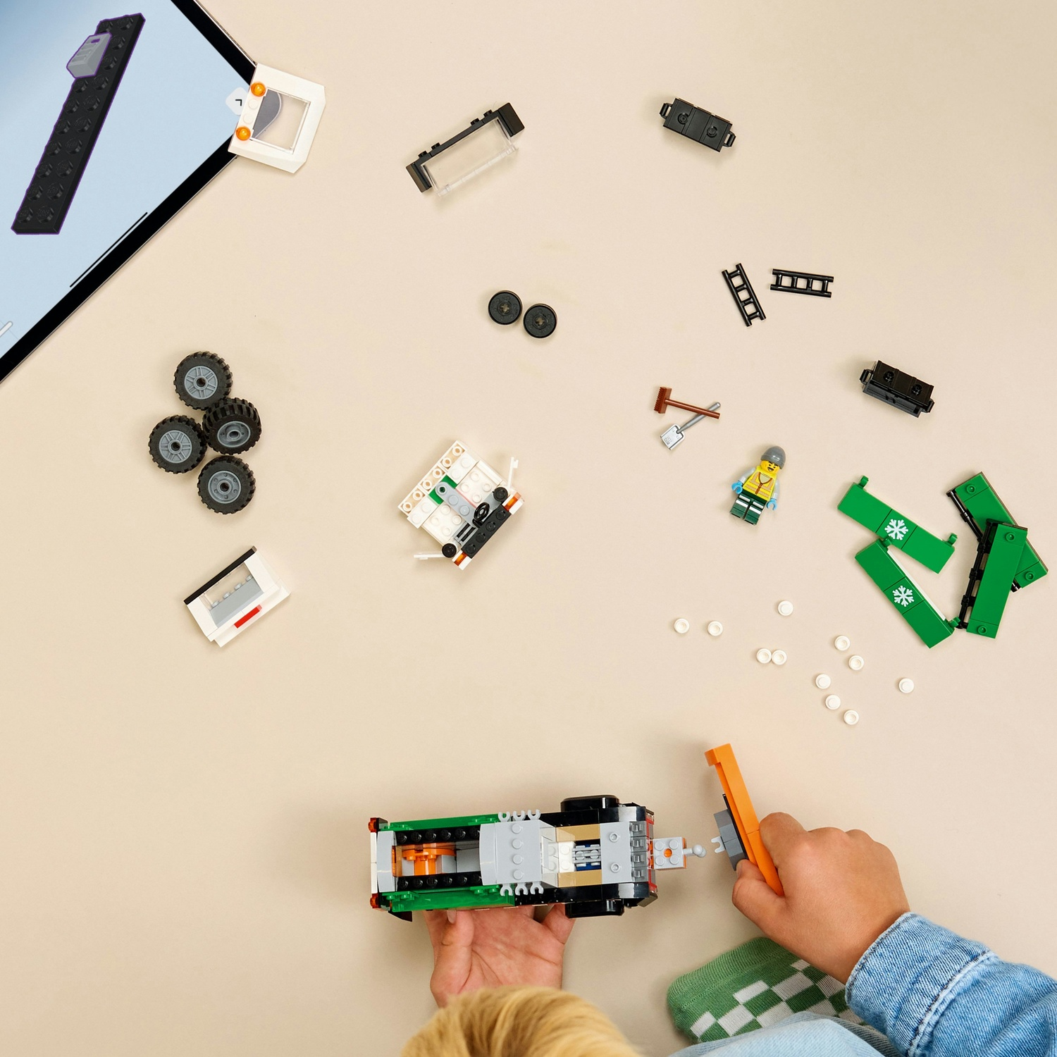 Un bambino costruisce un veicolo Lego verde con pezzi e istruzioni su un tavolo beige.