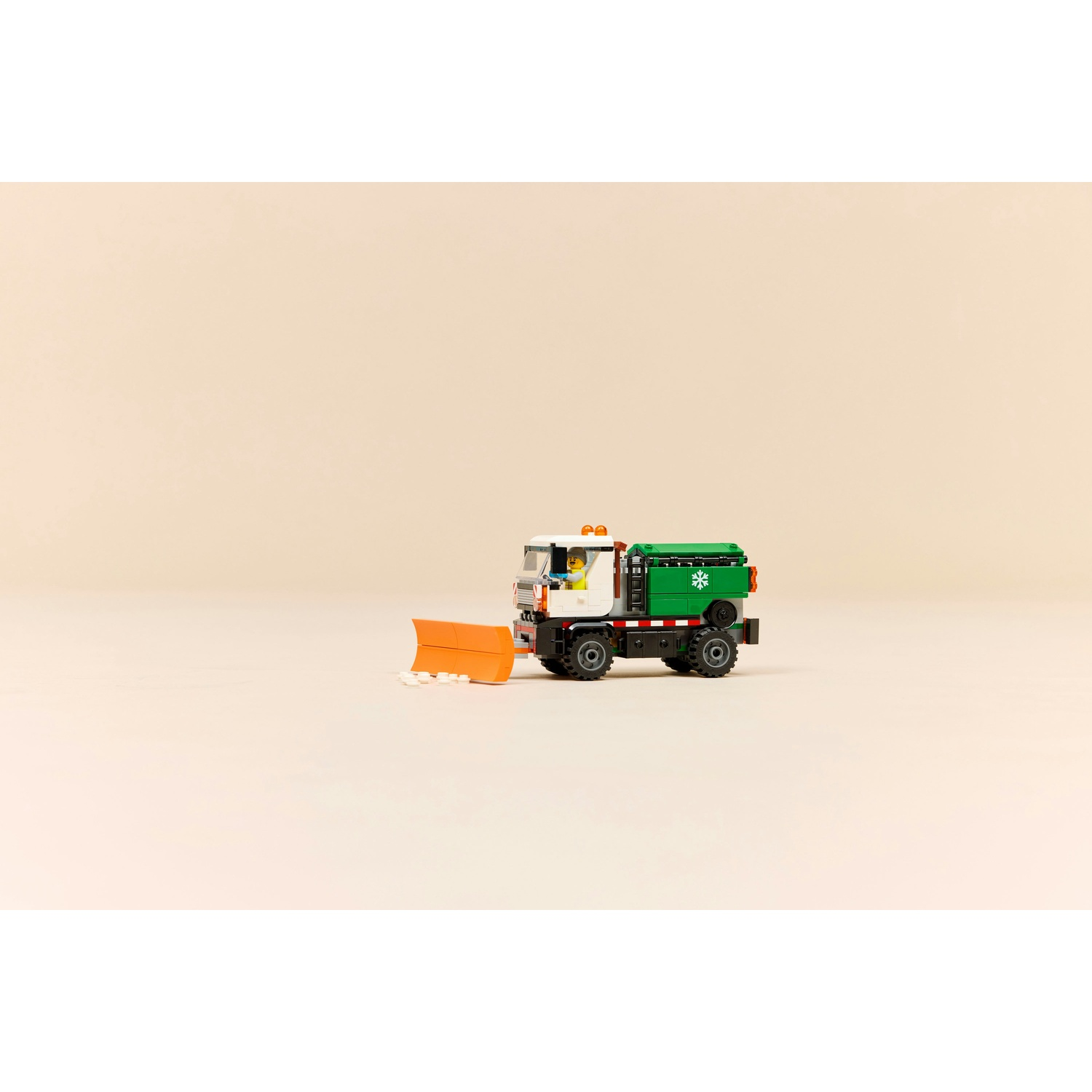 Uno spazzaneve Lego con corpo verde e lama arancione su sfondo chiaro.