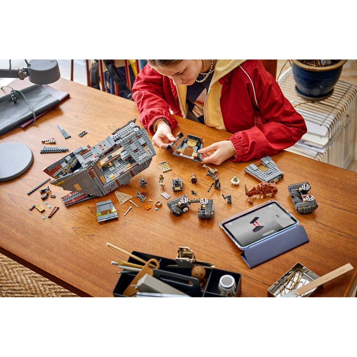 Un bambino costruisce modelli Lego su un tavolo di legno con un tablet.