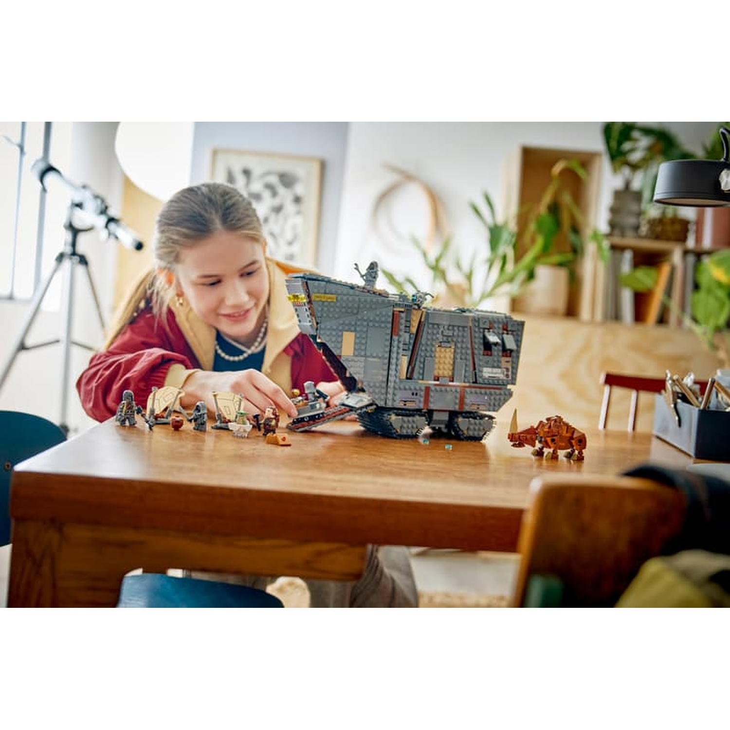 Una ragazza costruisce una grande base LEGO Star Wars grigia su un tavolo di legno con varie minifigure.