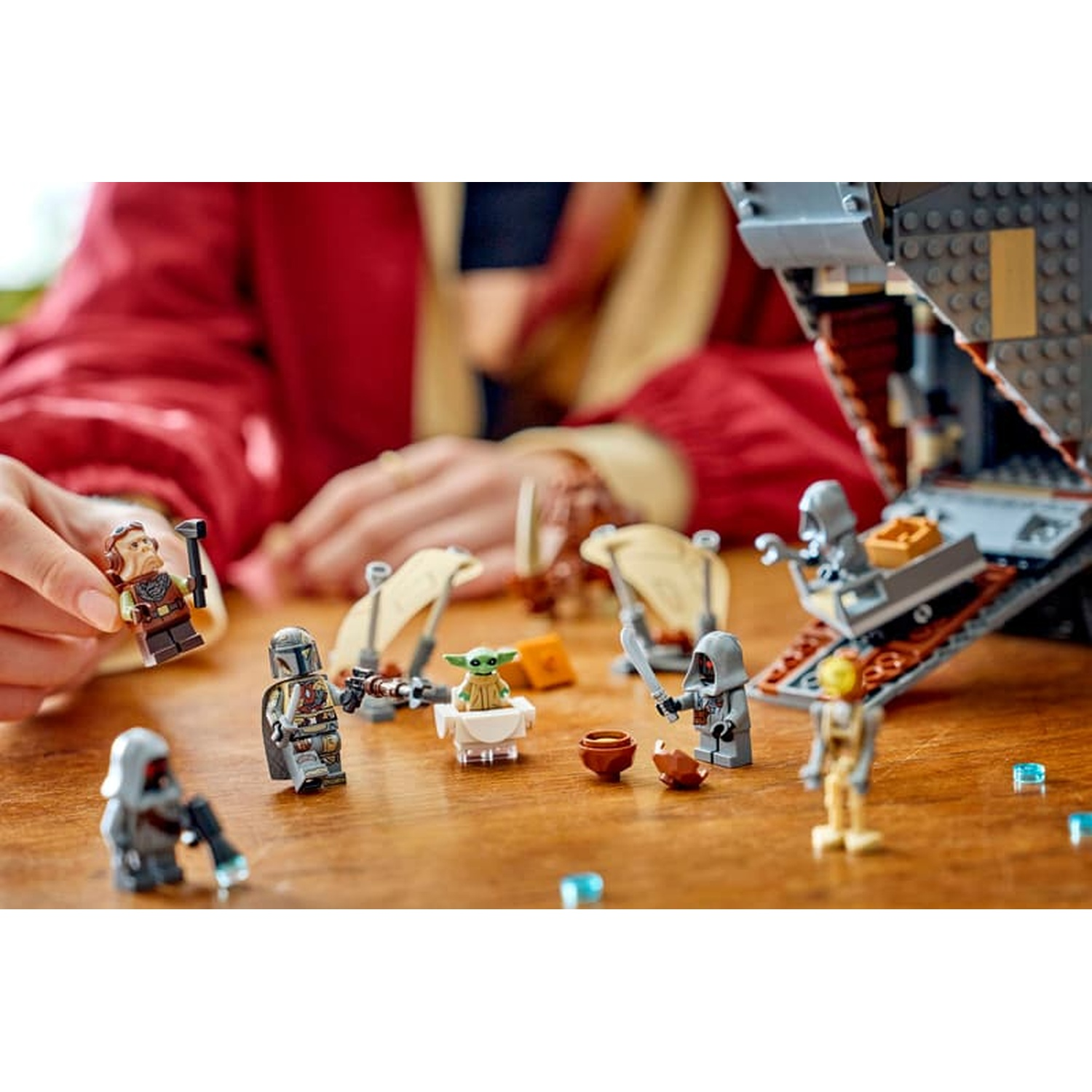 Persona che tiene una minifigura Lego con altre figure di Star Wars e nave su tavolo.
