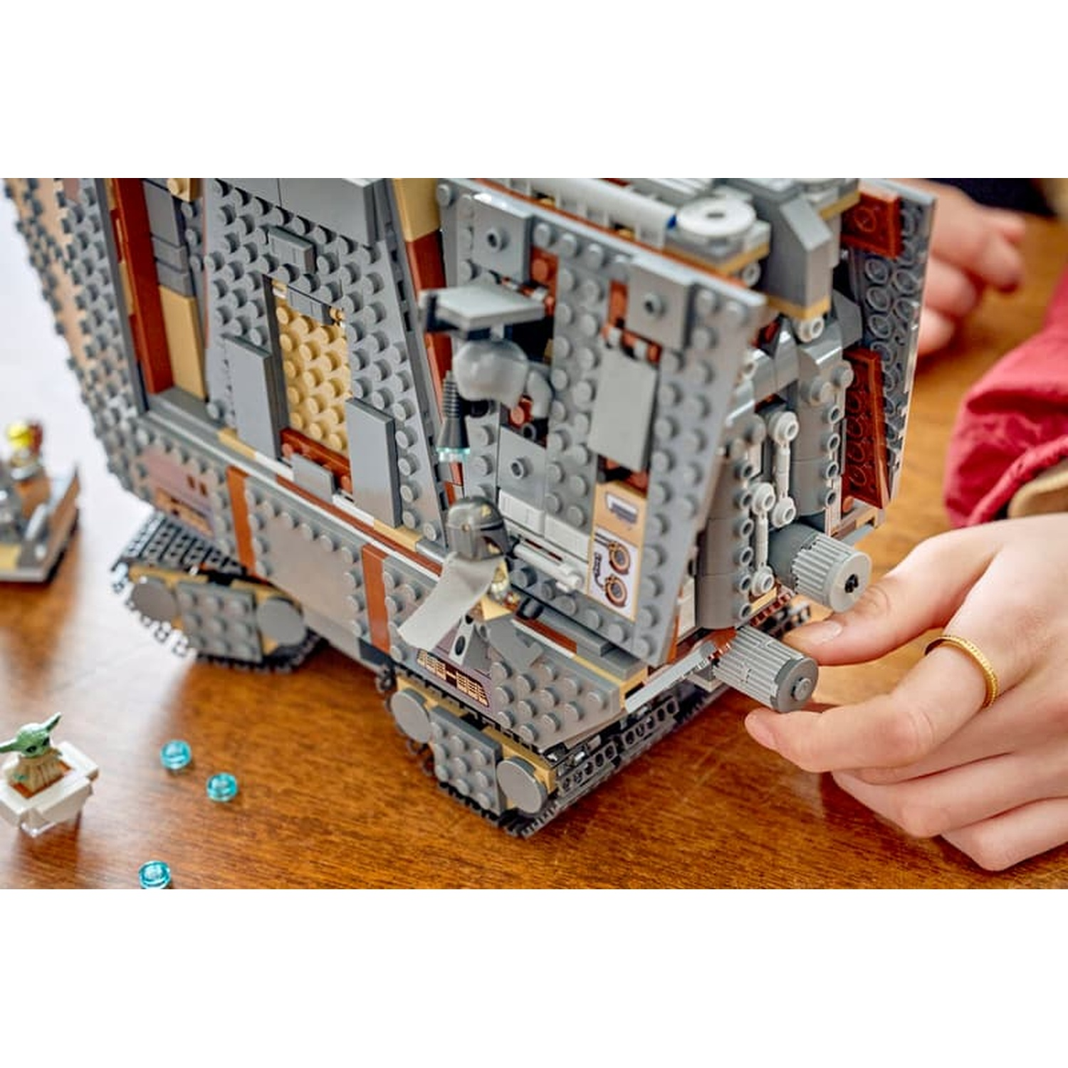 Una persona costruisce un complesso veicolo LEGO Star Wars grigio e marrone su un tavolo di legno.