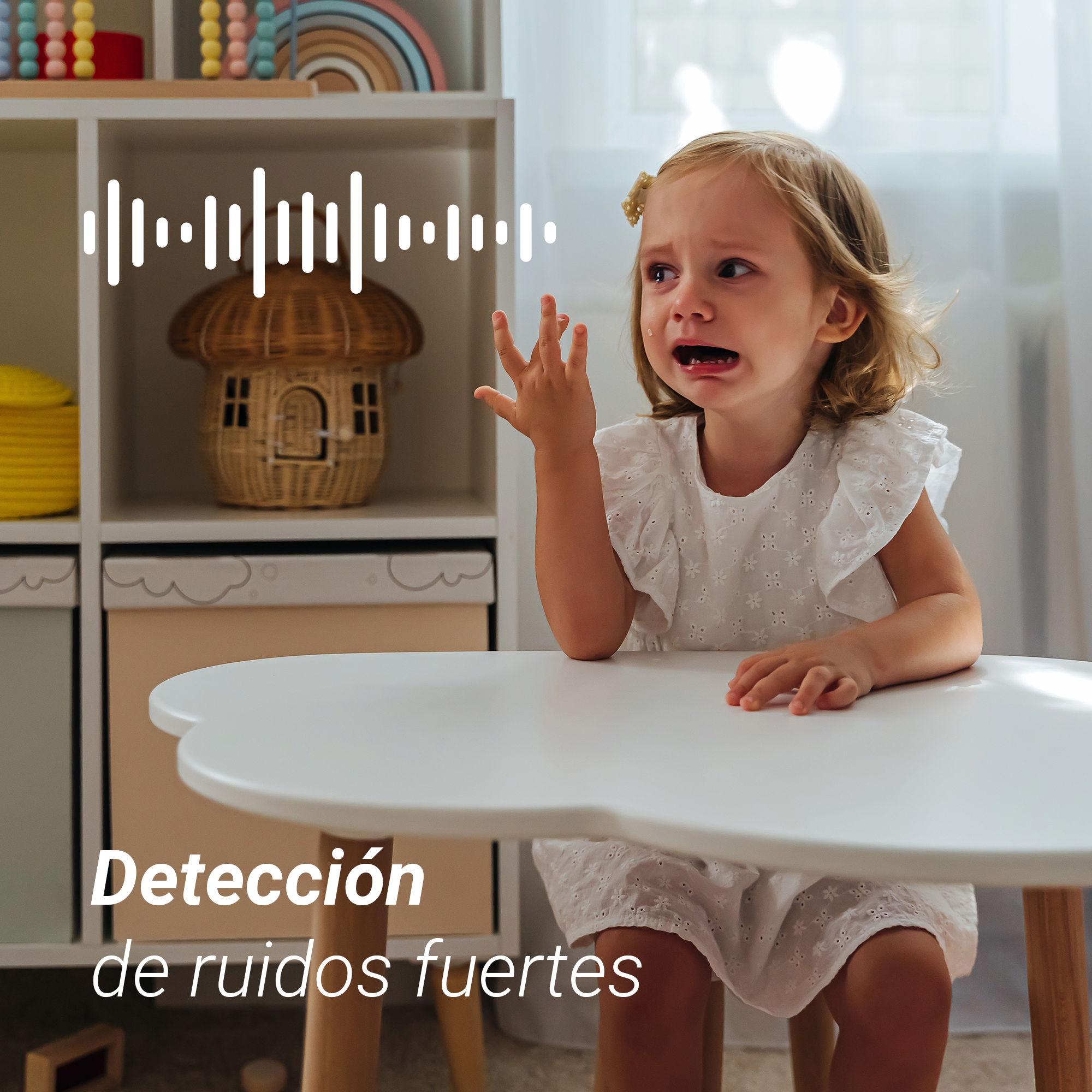 Un niño pequeño llorando se sienta en una mesa blanca frente a un estante de juguetes.