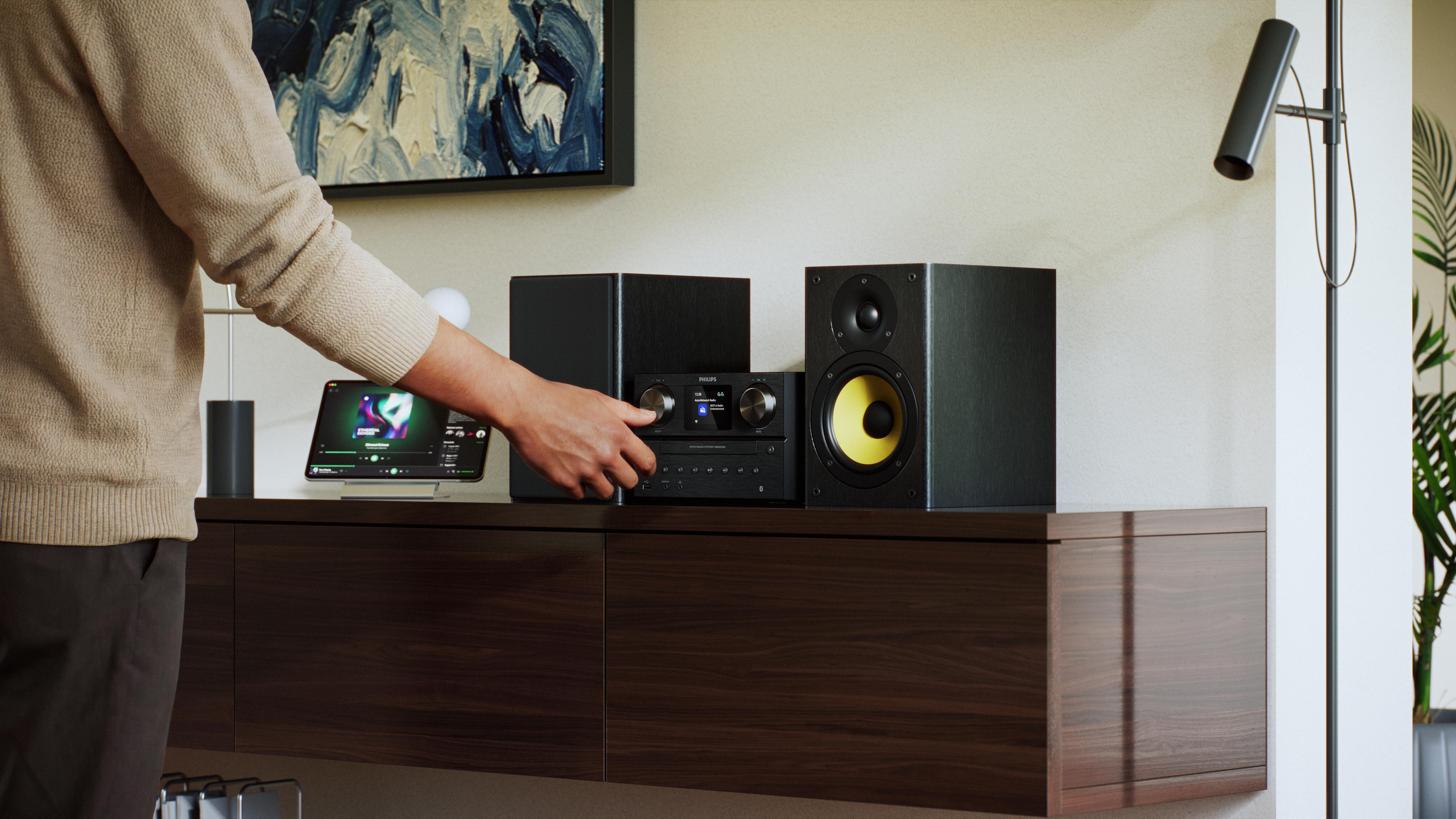 Eine Person stellt einen Philips-Musikplayer mit Lautsprechern auf einem Holztisch ein.