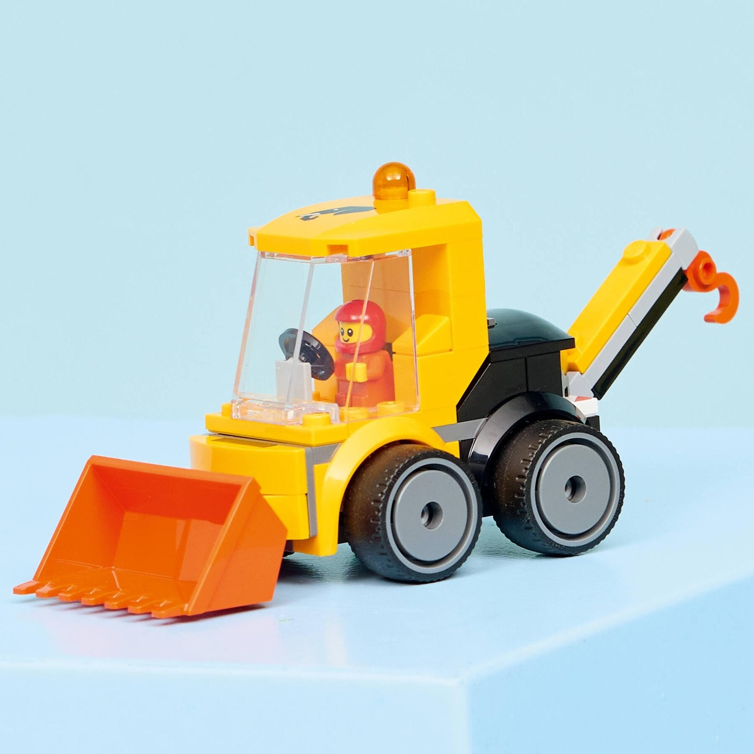 Un piccolo bulldozer Lego giallo con benna arancione e braccio gru su sfondo azzurro.