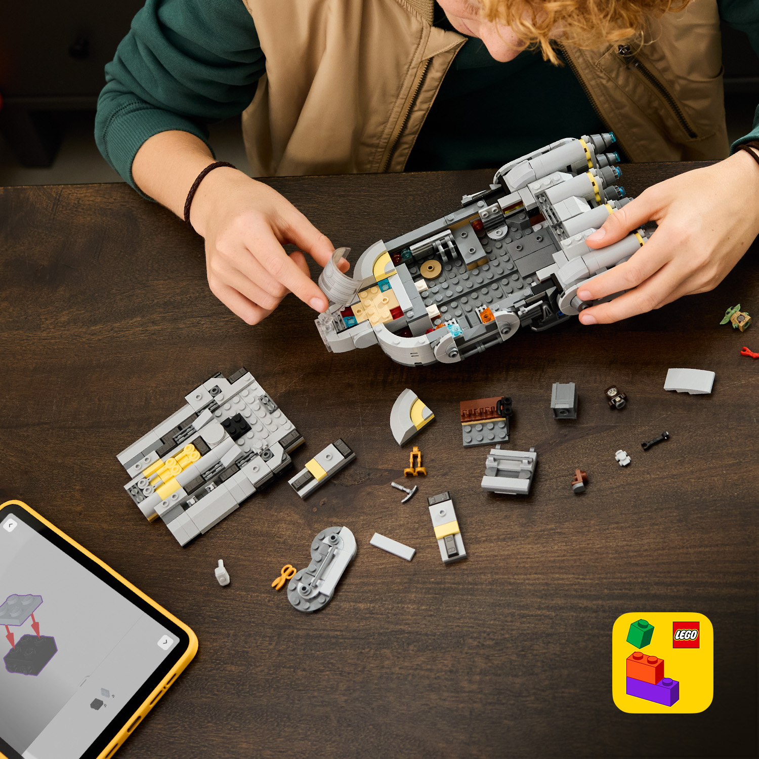 Una persona costruisce un'astronave Lego su un tavolo di legno con istruzioni su tablet.
