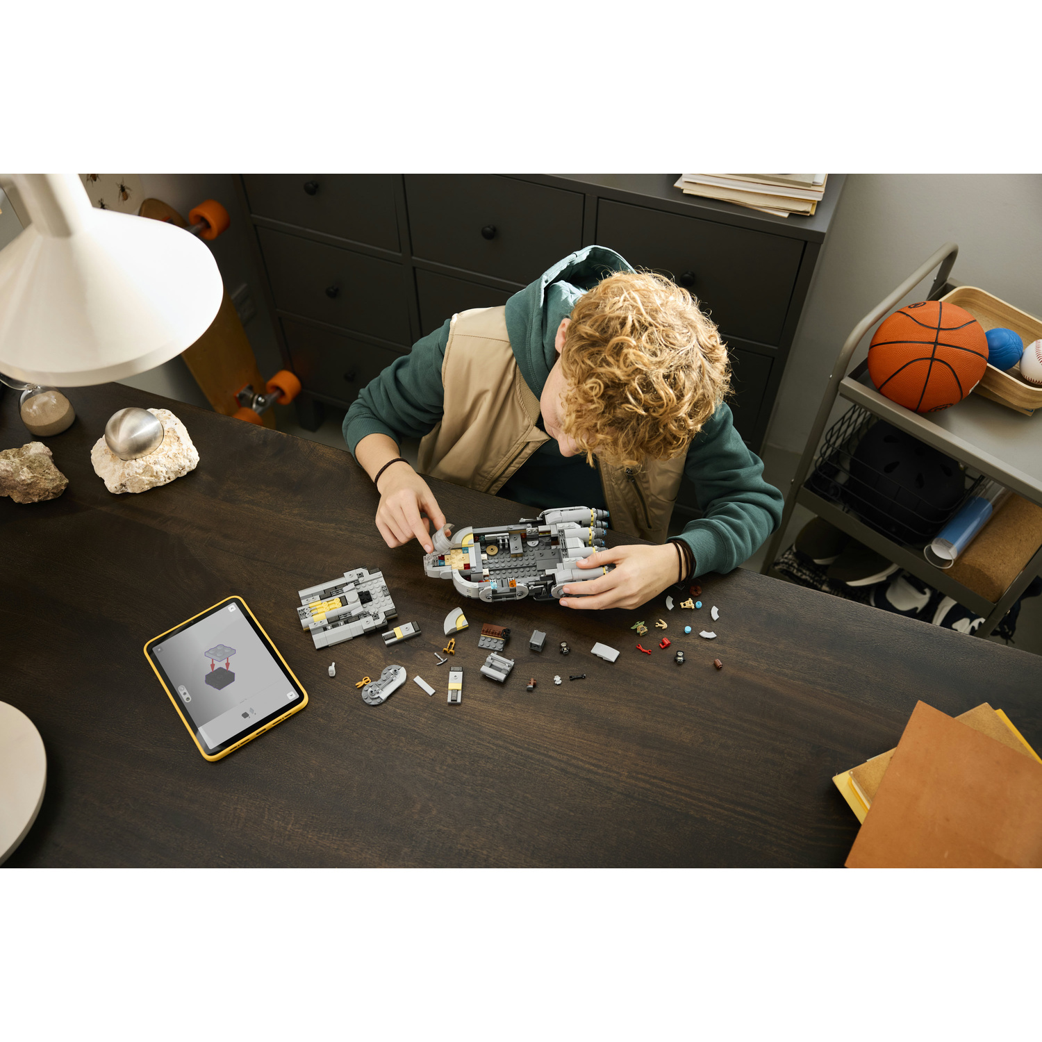 Un ragazzo costruisce un modello Lego su una scrivania di legno scuro, guidato da un tablet.