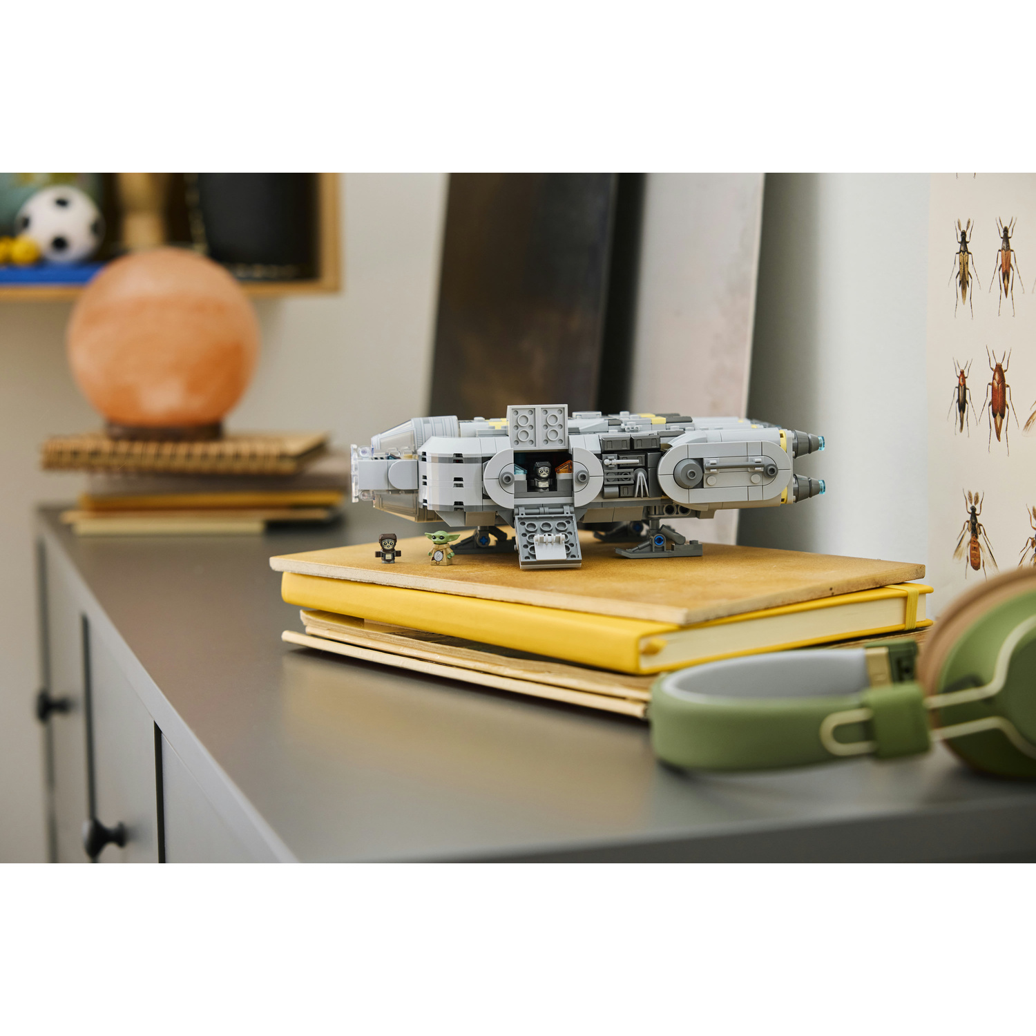 Una nave spaziale Lego grigia si trova su libri gialli su una scrivania accanto a cuffie verdi.