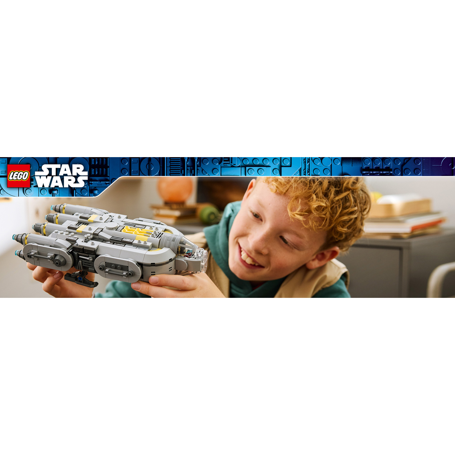 Un ragazzo tiene in mano un'astronave grigia Lego Star Wars e sorride.