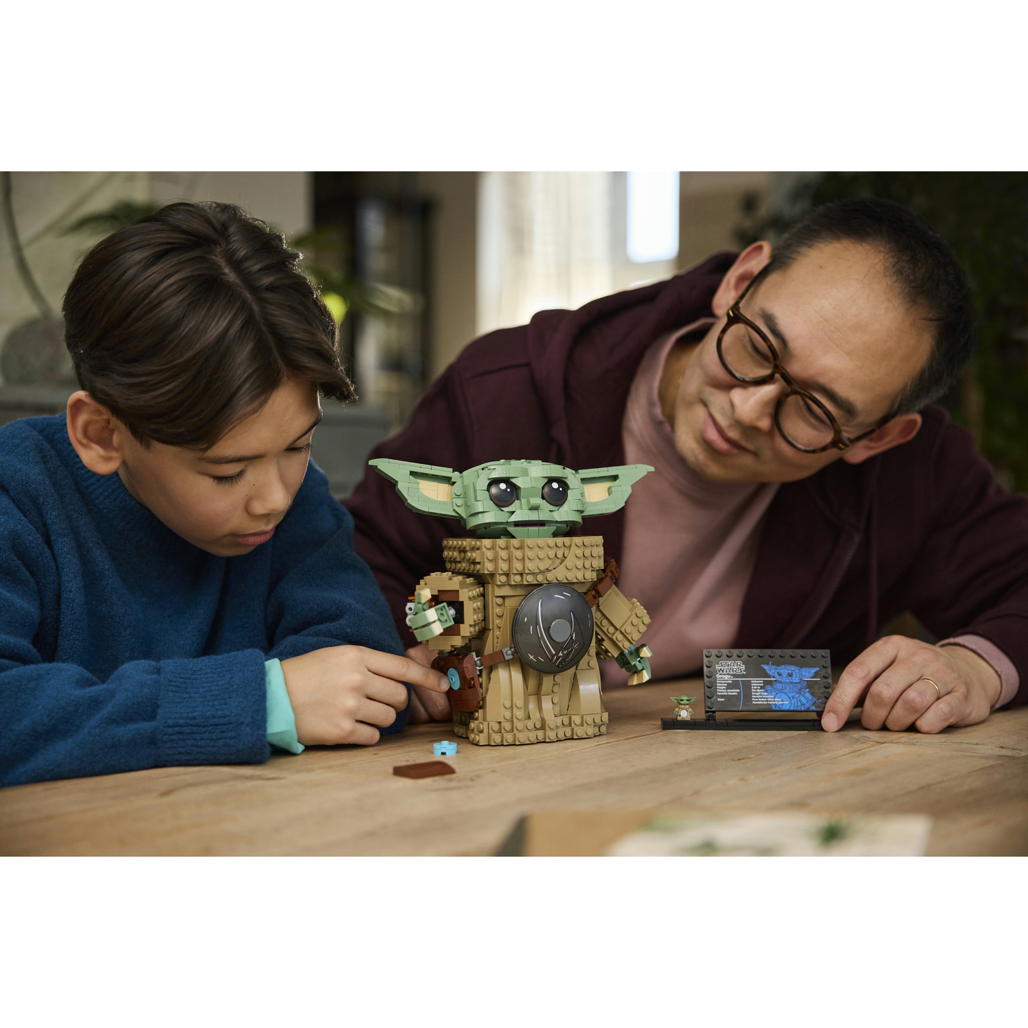 Un ragazzo e un uomo seduti a un tavolo costruiscono insieme una figura Lego Star Wars Grogu.