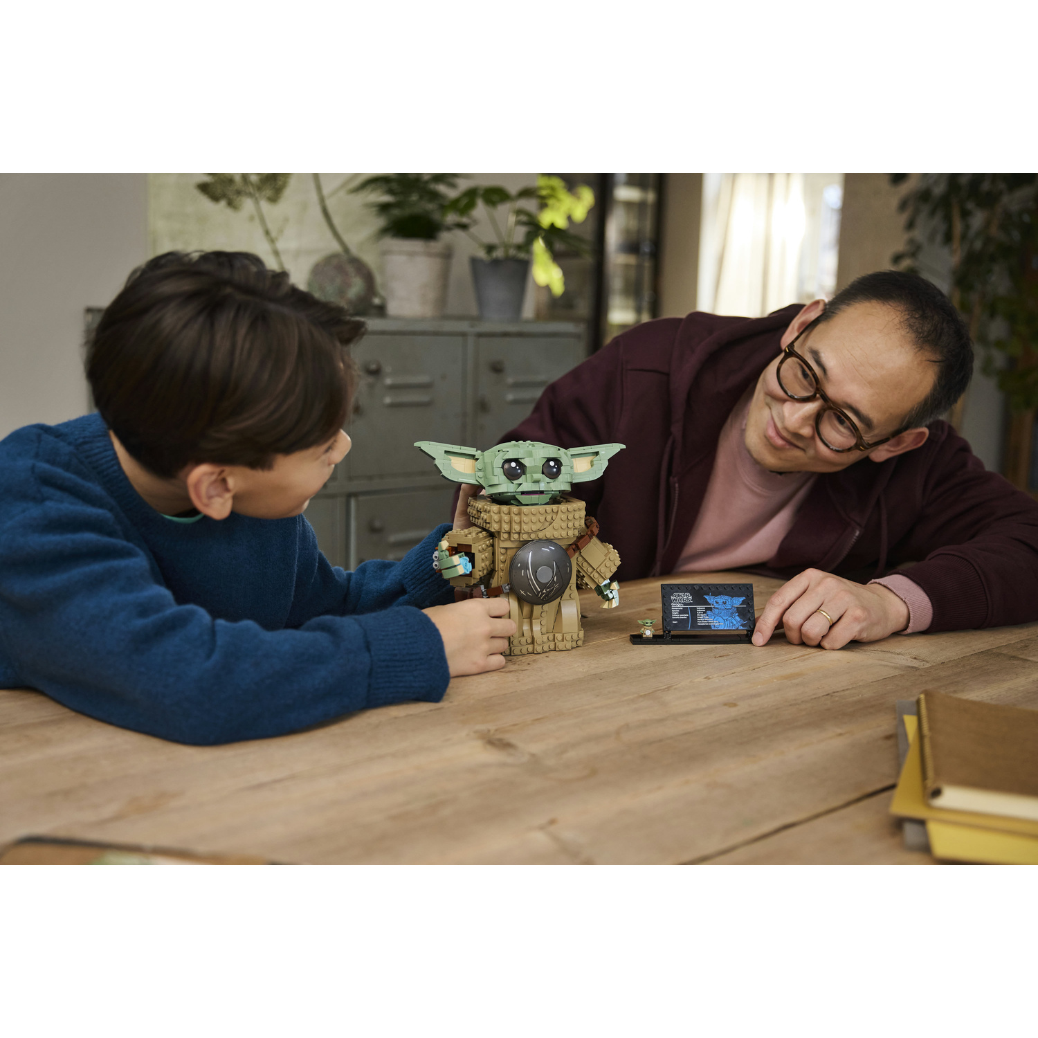 Un ragazzo e un uomo assemblano insieme una figura LEGO Star Wars su un tavolo di legno.