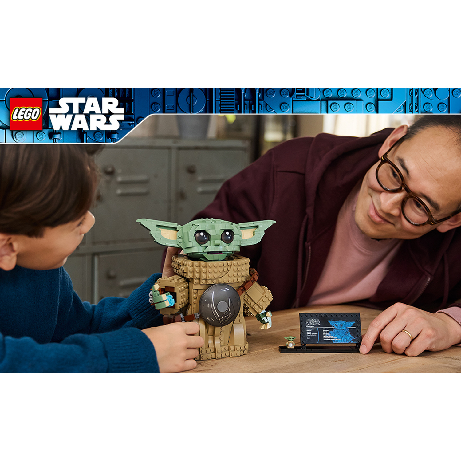 Un uomo e un ragazzo giocano insieme con una statuetta LEGO Star Wars Grogu su un tavolo di legno.