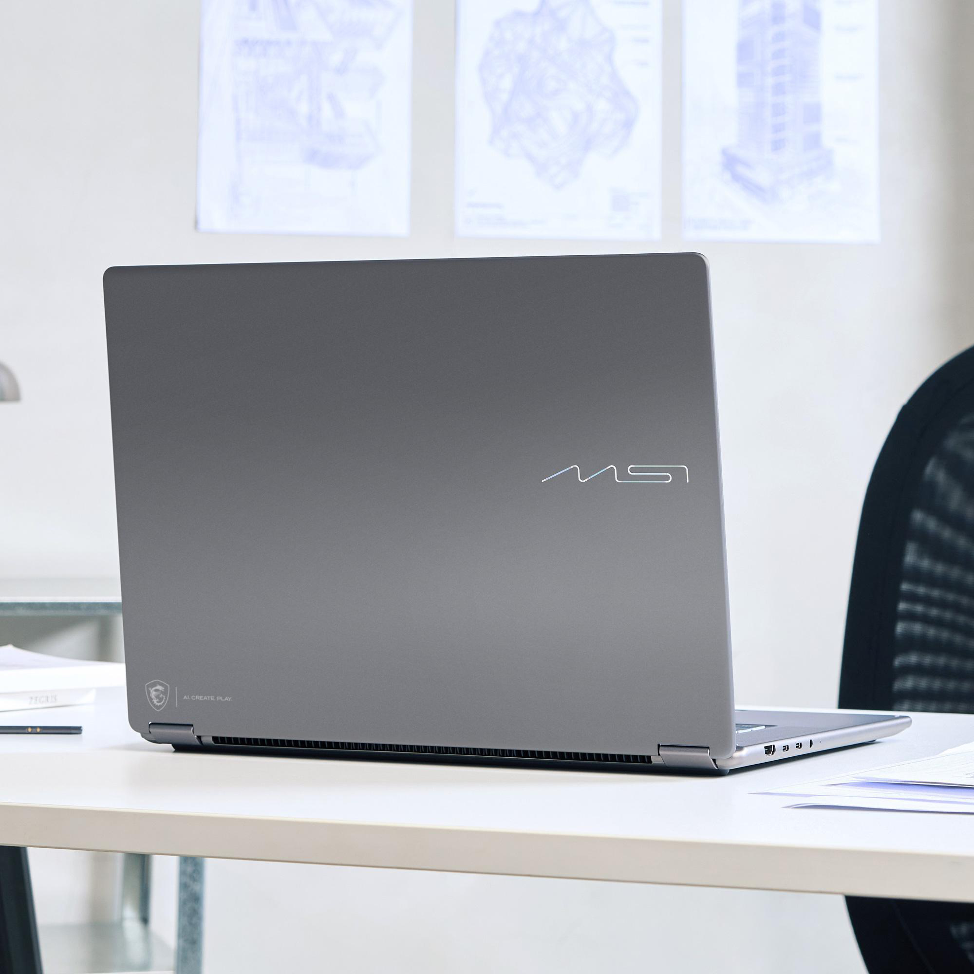 Ein grauer MSI-Laptop steht auf einem weißen Schreibtisch in einem modernen Büro vor technischen Zeichnungen an der Wand.