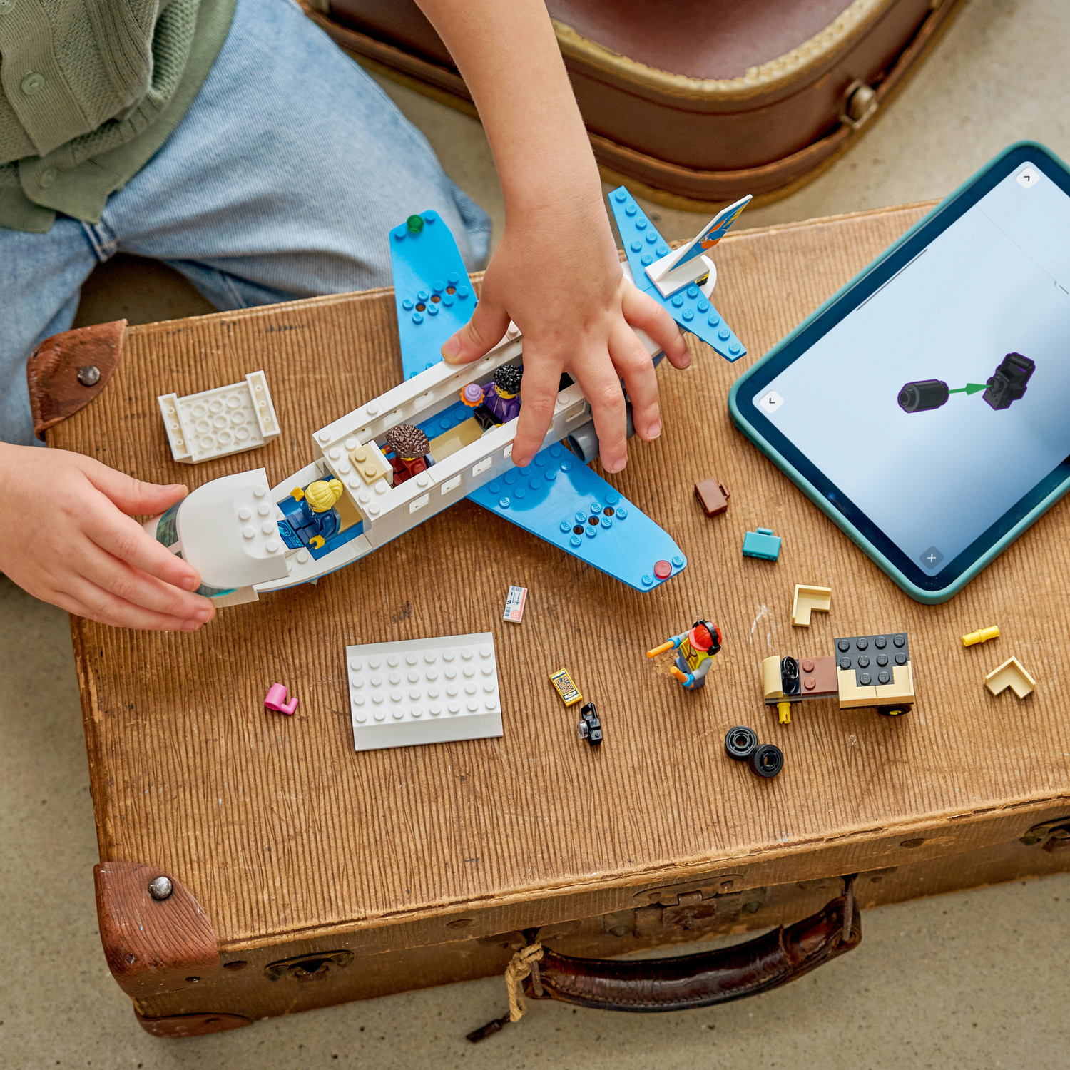 Un bambino costruisce un aereo Lego su una vecchia valigia accanto a un tablet.