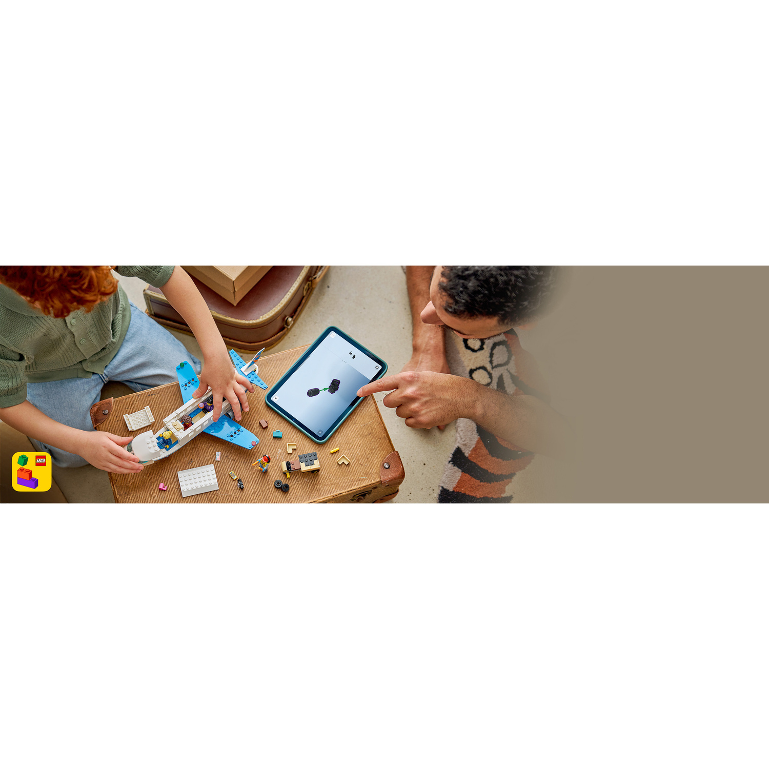 Un bambino costruisce un aereo Lego mentre un uomo indica un tablet con le istruzioni.