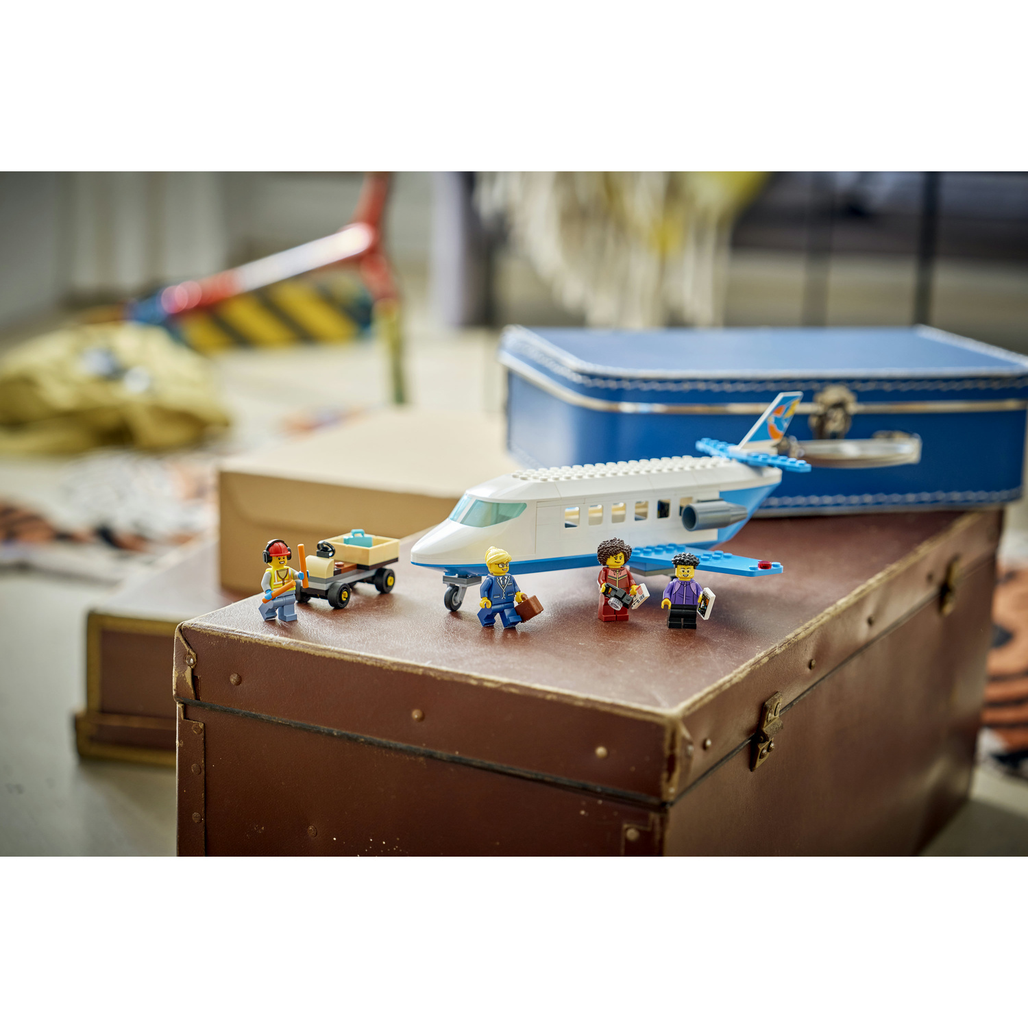 Aereo passeggeri Lego e minifigure su un baule marrone davanti a una scatola blu.