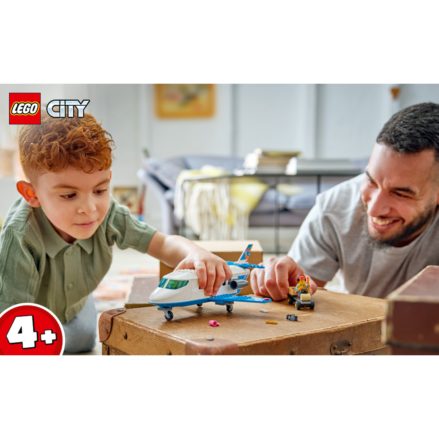 Un bambino e un uomo giocano con un aereo Lego City su una vecchia valigia in un soggiorno.