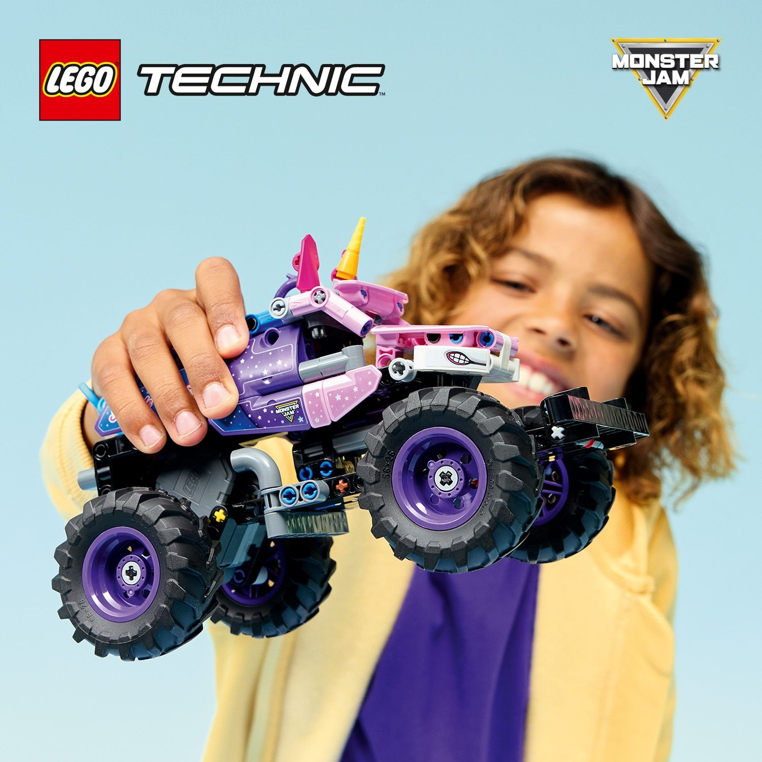 Un bambino tiene con orgoglio un camion giocattolo Lego Technic Monster Jam viola e rosa.