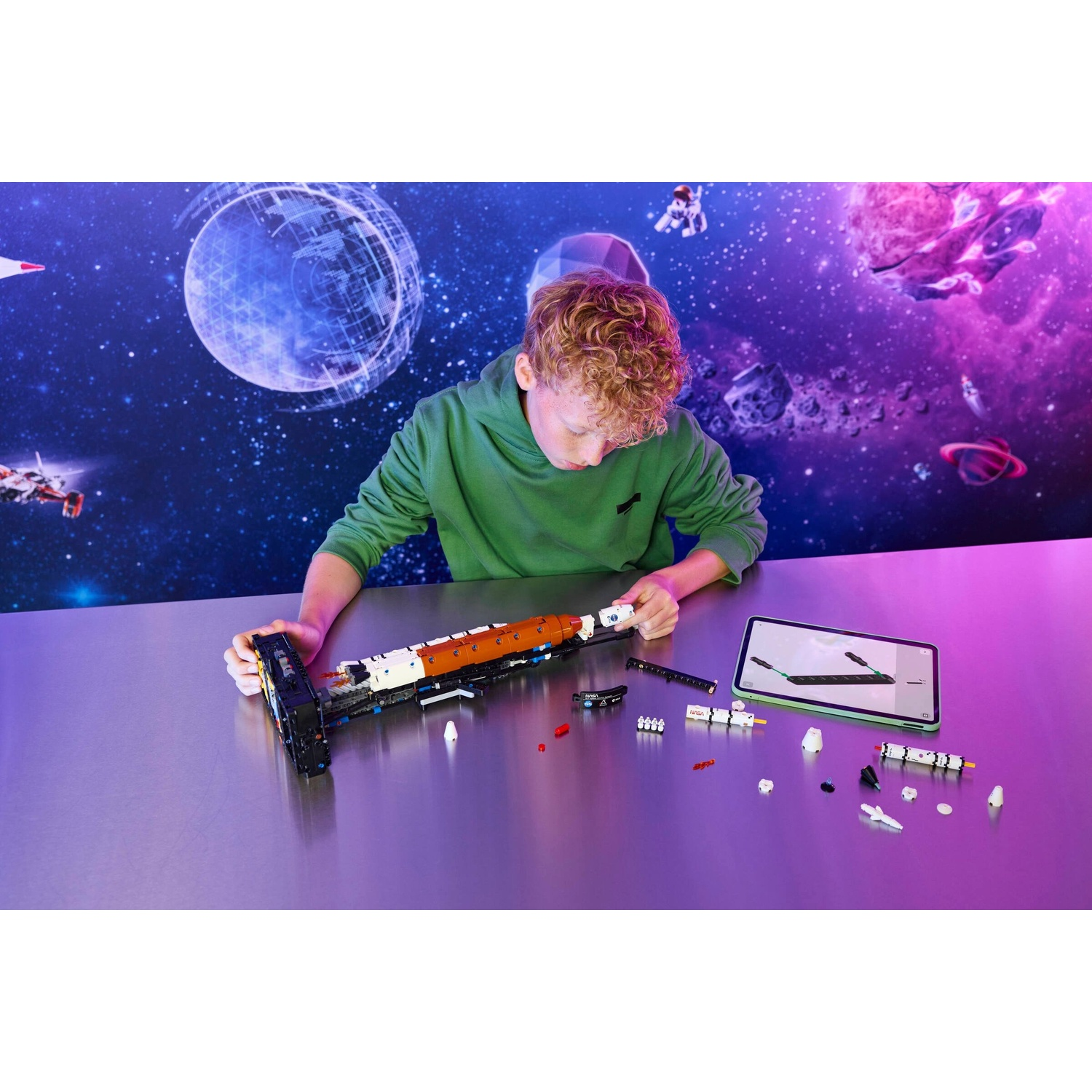 Un ragazzo costruisce un'astronave LEGO su un tavolo davanti a uno sfondo spaziale con tablet.
