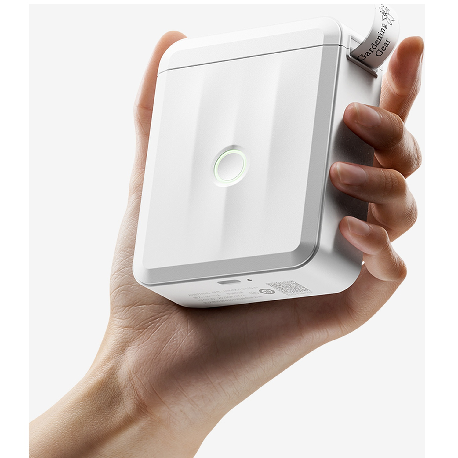 A hand holds a compact white portable printer, printing a small label against a plain background.