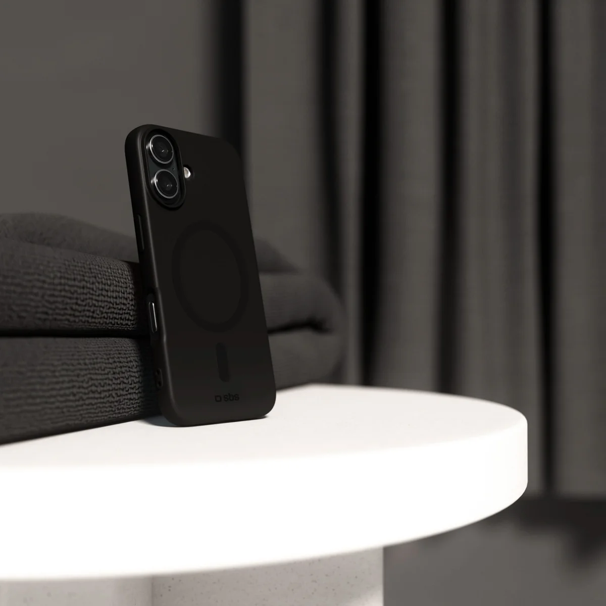 Czarny smartfon w etui stoi na białym stole na tle ciemnych zasłon.