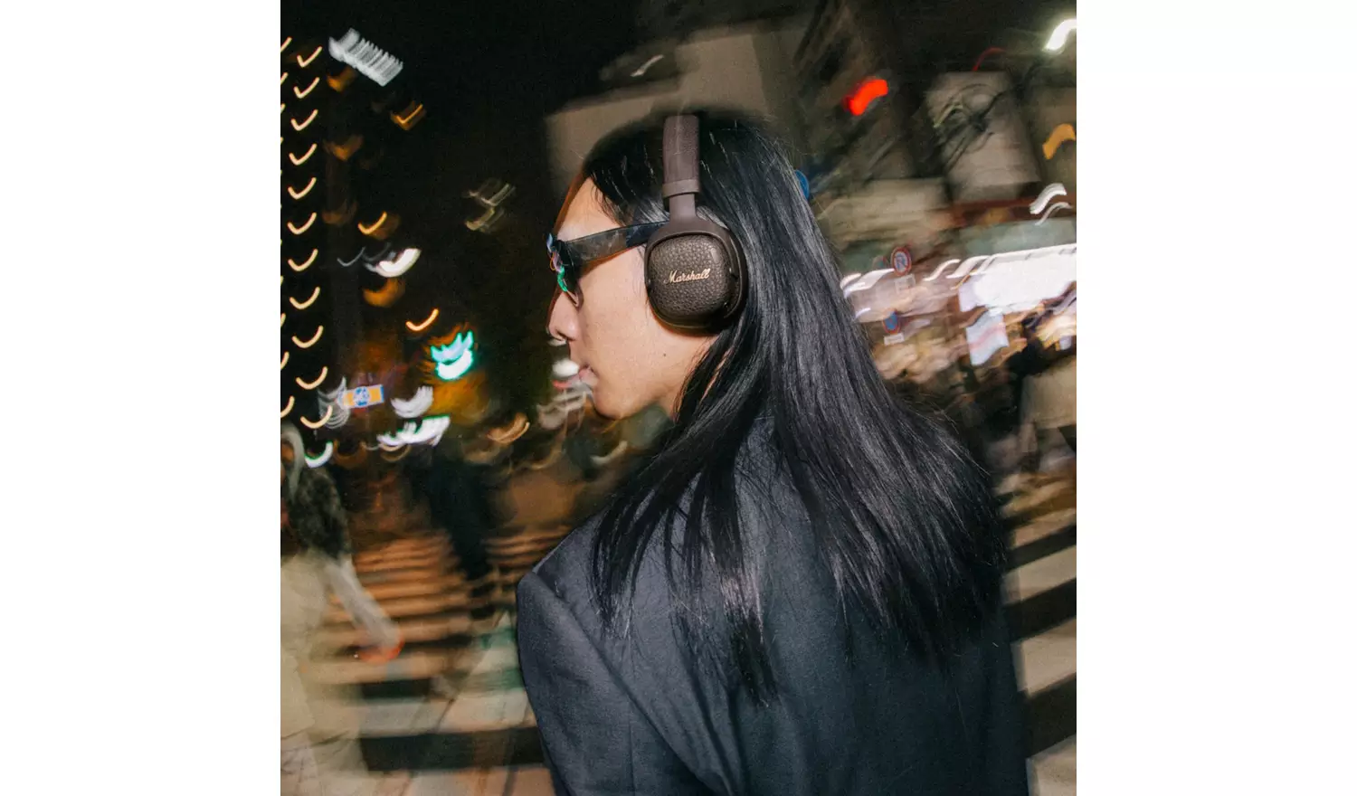Persona con cabello largo y oscuro y auriculares caminando por una calle concurrida de noche.