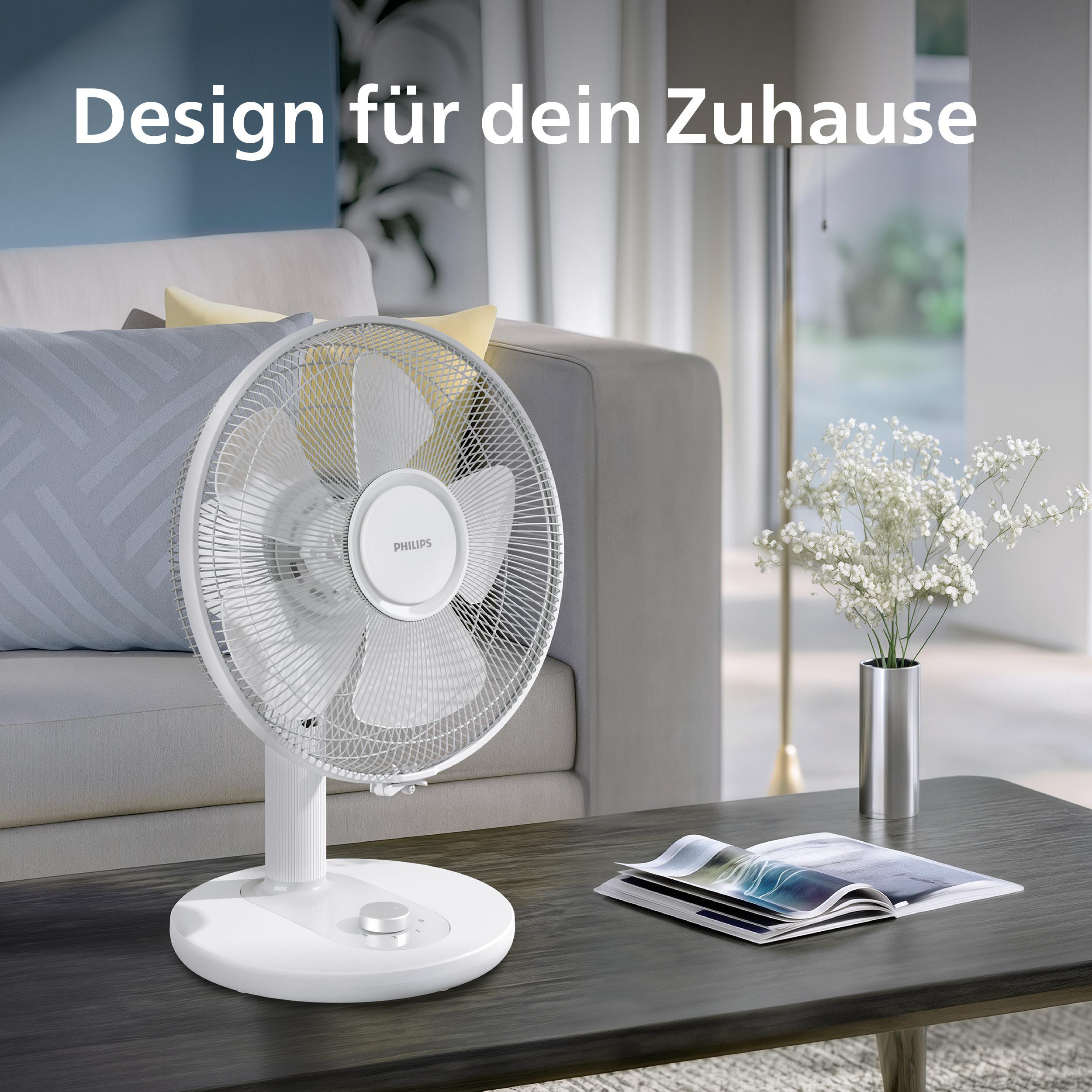 Ein weißer Philips Tischventilator steht auf einem dunklen Holztisch in einem modernen Wohnzimmer mit Sofa.