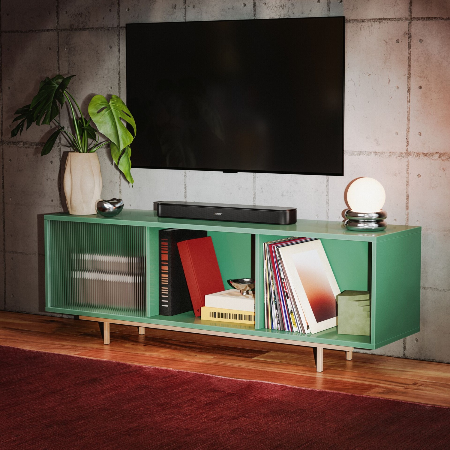 Ein grünes TV-Möbel mit Büchern und einer Soundbar steht an einer Betonwand, darüber ein Fernseher.