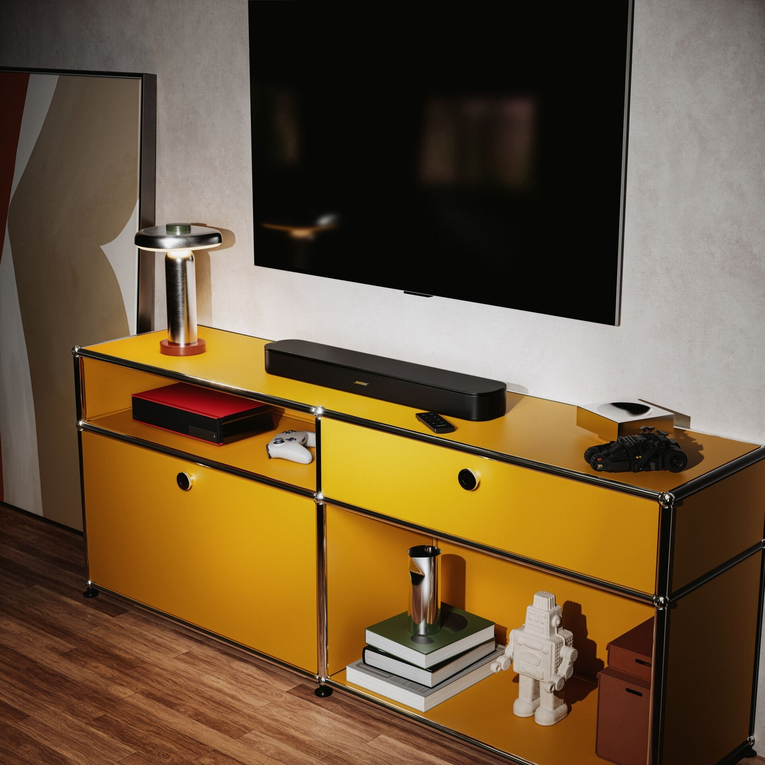 Ein gelbes Sideboard mit Fernseher an der Wand, Soundbar, Lampe und Dekoartikeln auf holzfarbenem Boden.