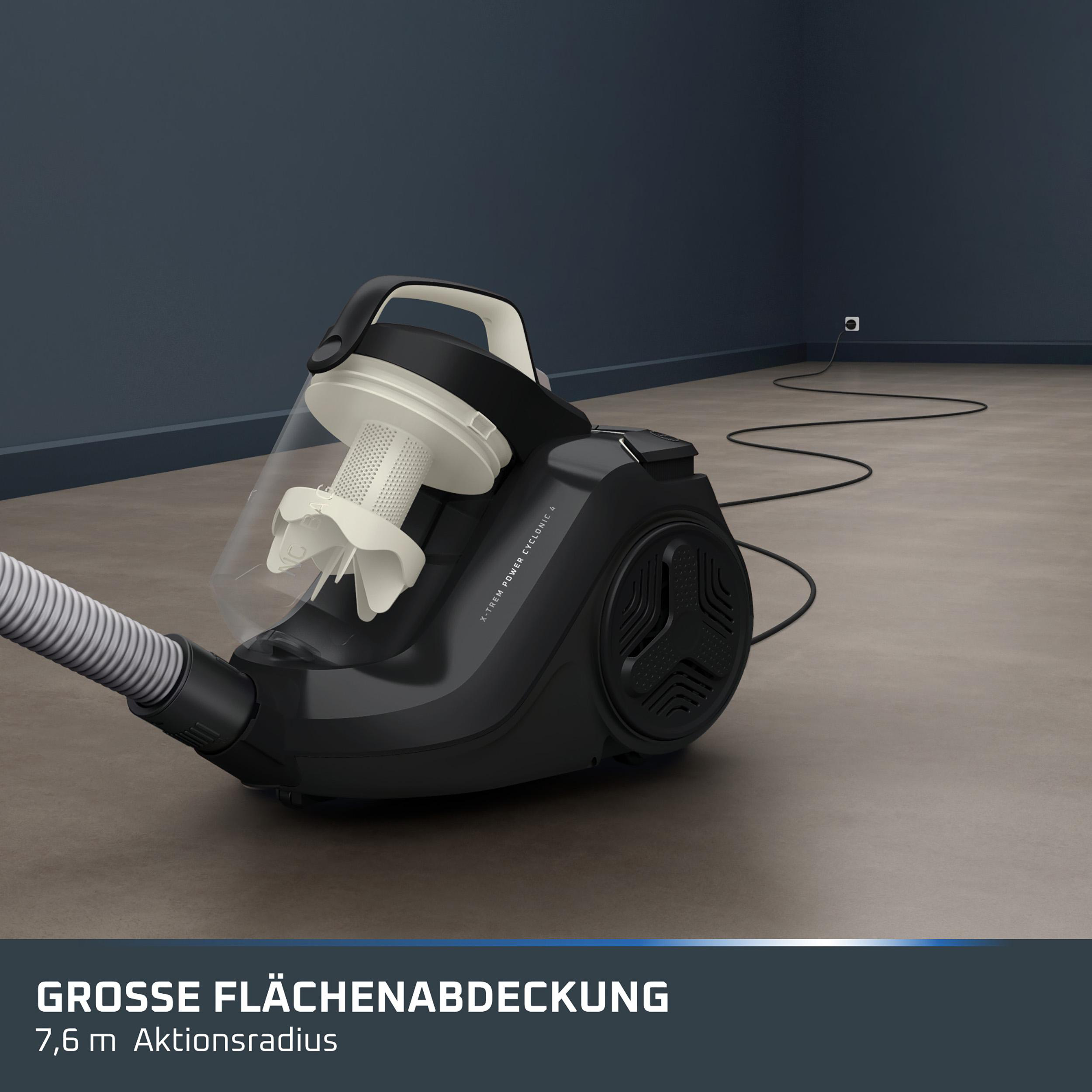 Schwarzer Staubsauger mit klarem Staubbehälter auf grauem Boden, angeschlossen an eine Steckdose an der Wand.