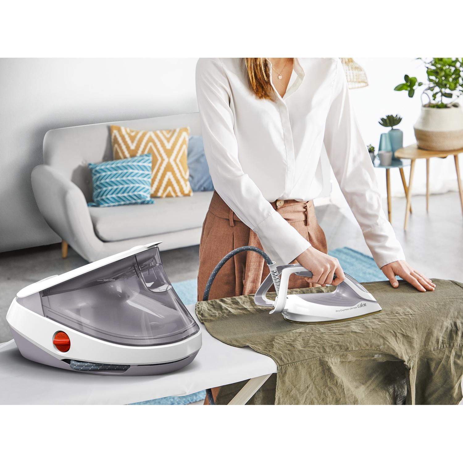Woman ironing clothes with a white steam generator iron in a bright living room.