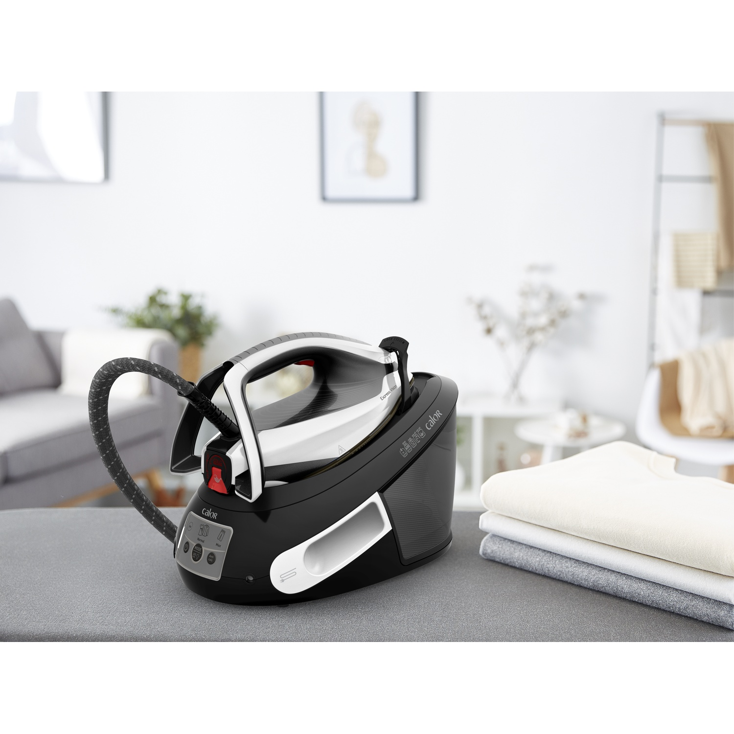 Black steam generator iron on a table next to folded laundry in a bright room.
