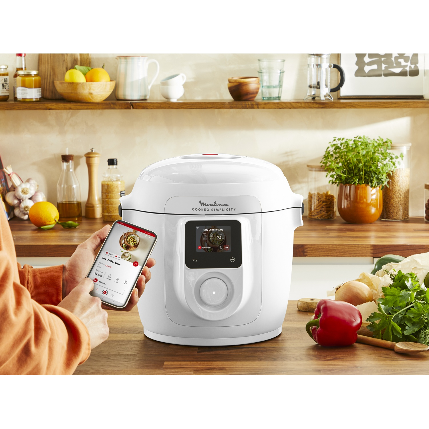 Een witte Moulinex Cookeo Simplicity multicooker op een houten aanrecht met een smartphone met recepten-app.