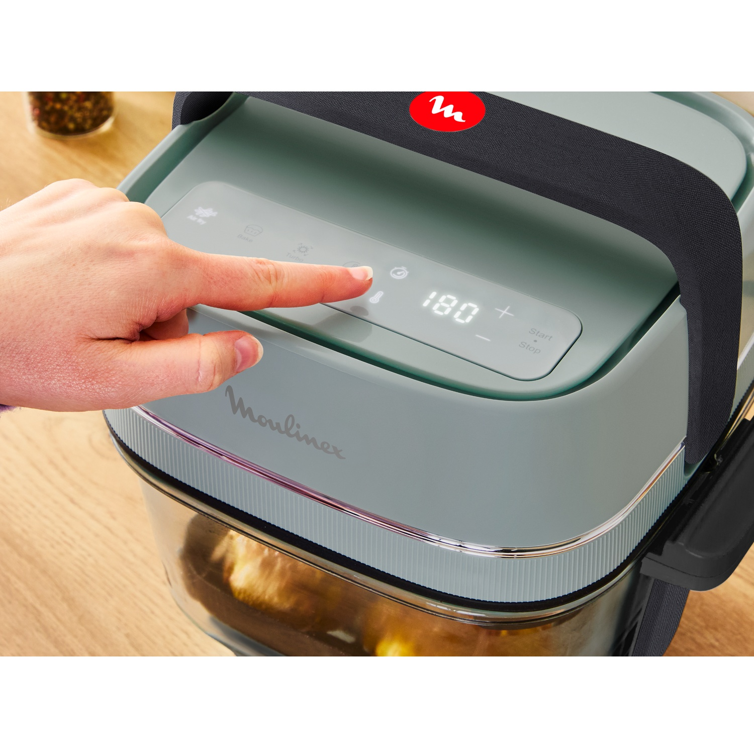Een vinger drukt op het digitale bedieningspaneel van een groene Moulinex airfryer op 180 graden.