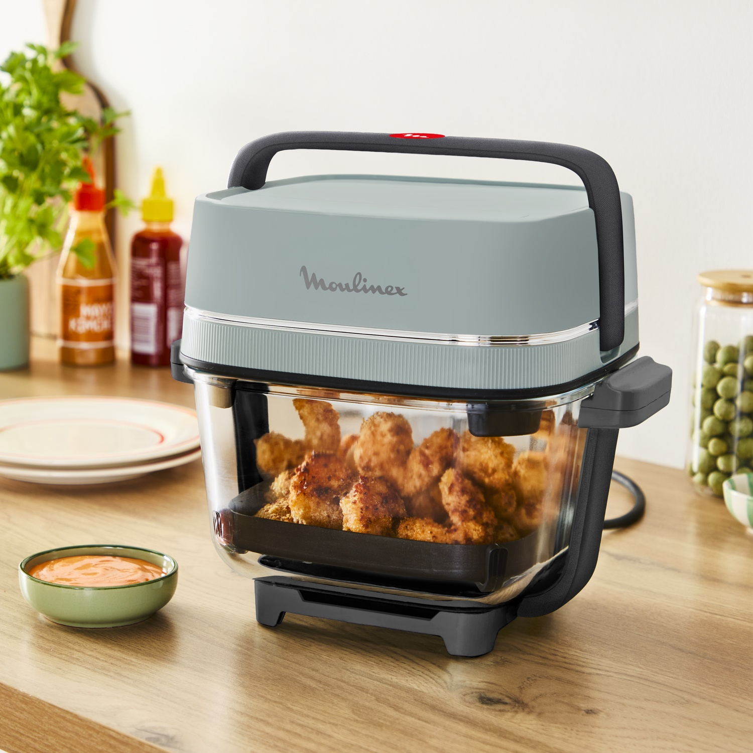 Moulinex heteluchtfriteuse met glazen kom met gepaneerde kipstukjes op een aanrecht.