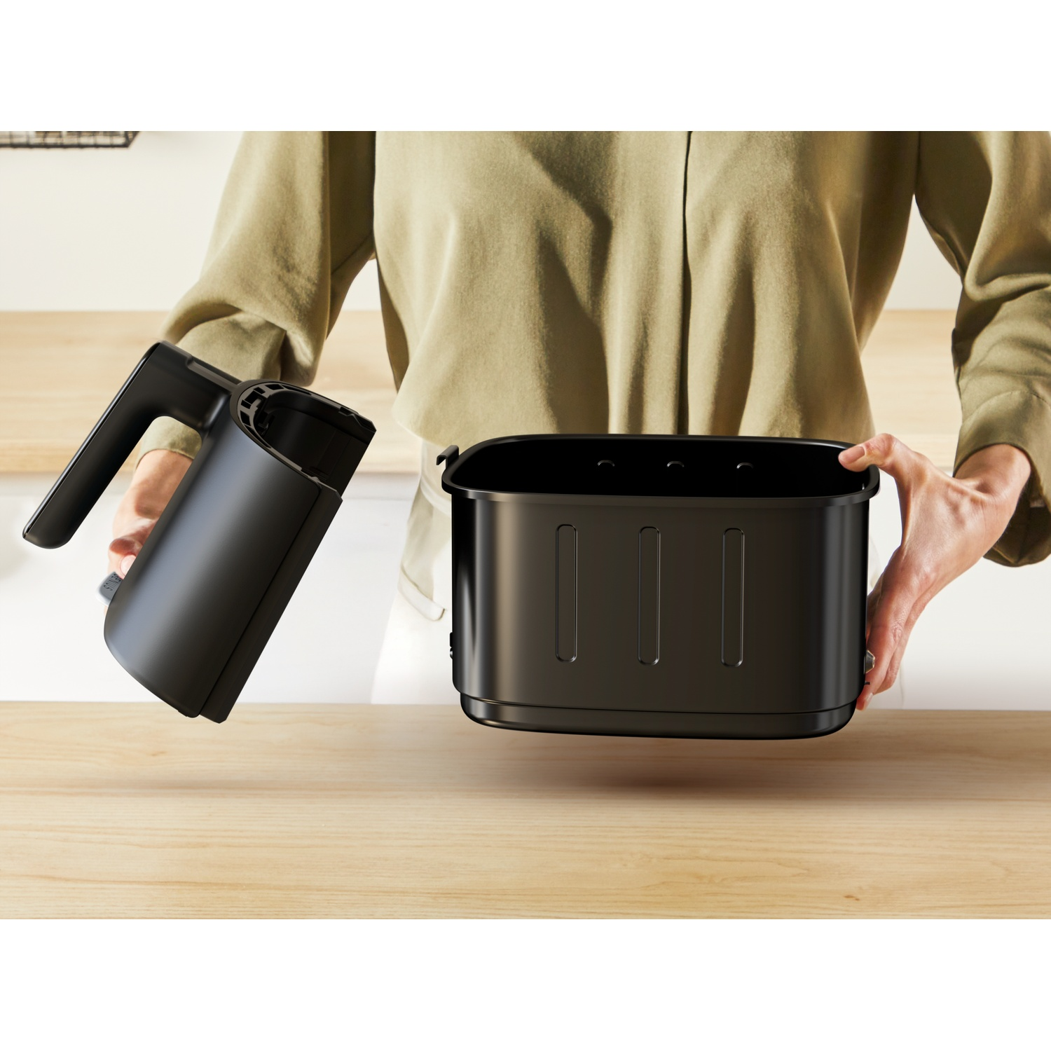 Iemand houdt twee delen van een zwarte airfryer mand boven een houten aanrecht.