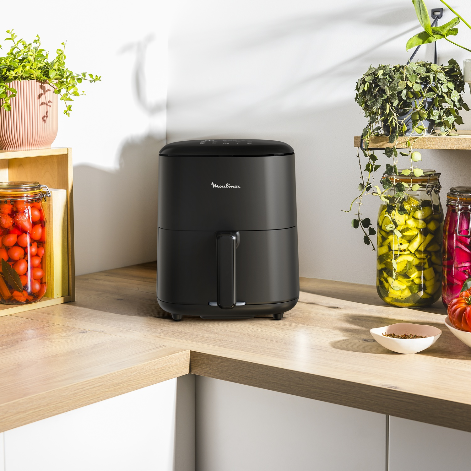 Zwarte Moulinex heteluchtfriteuse op een houten aanrecht met planten en potten.
