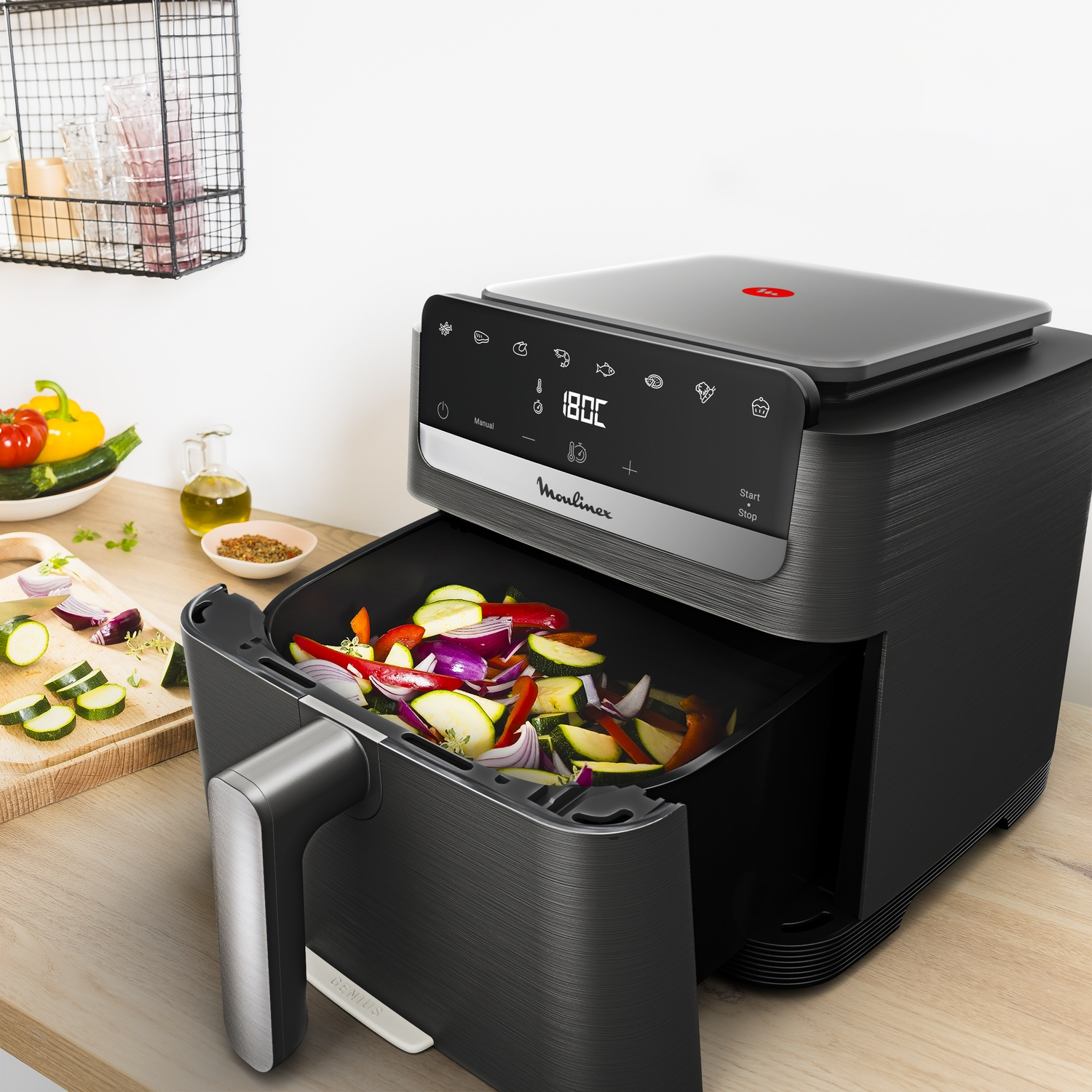 Zwarte Moulinex heteluchtfriteuse op houten aanrecht met open lade vol groenten, naast verse producten.