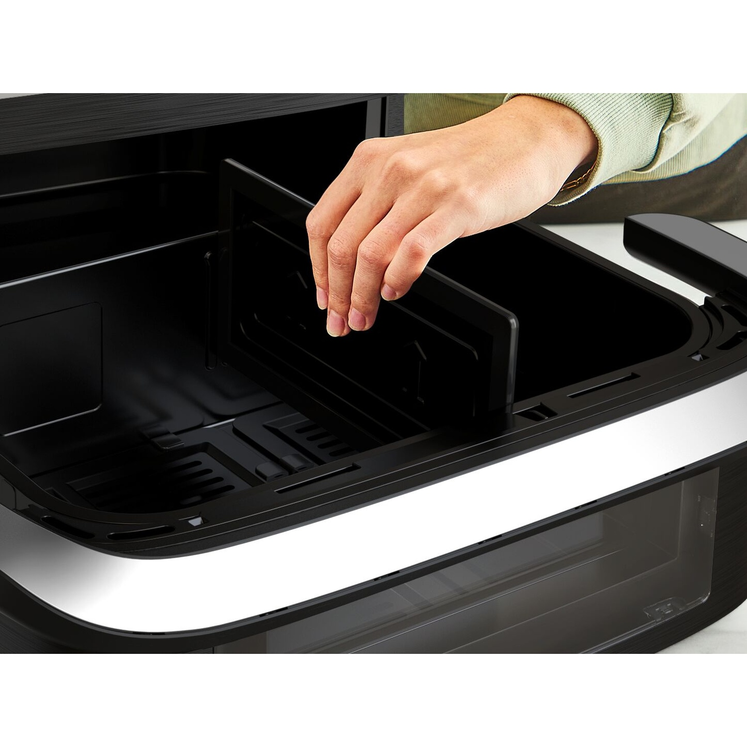 Een hand plaatst een zwarte verdeler in de frituurmand van een airfryer.