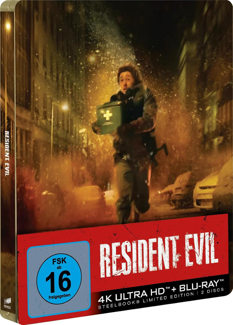 Ein Mann läuft mit einem Erste-Hilfe-Kasten durch eine brennende Straße auf einem Resident Evil Steelbook-Cover.