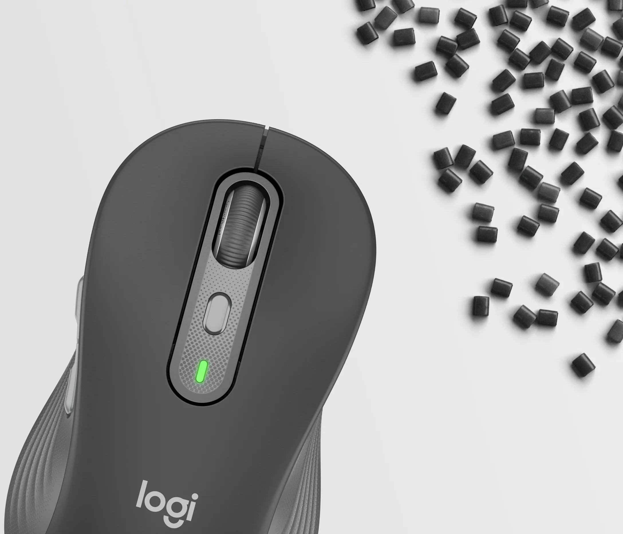 Une souris d'ordinateur Logi grise sur fond blanc près de pastilles en plastique noir.