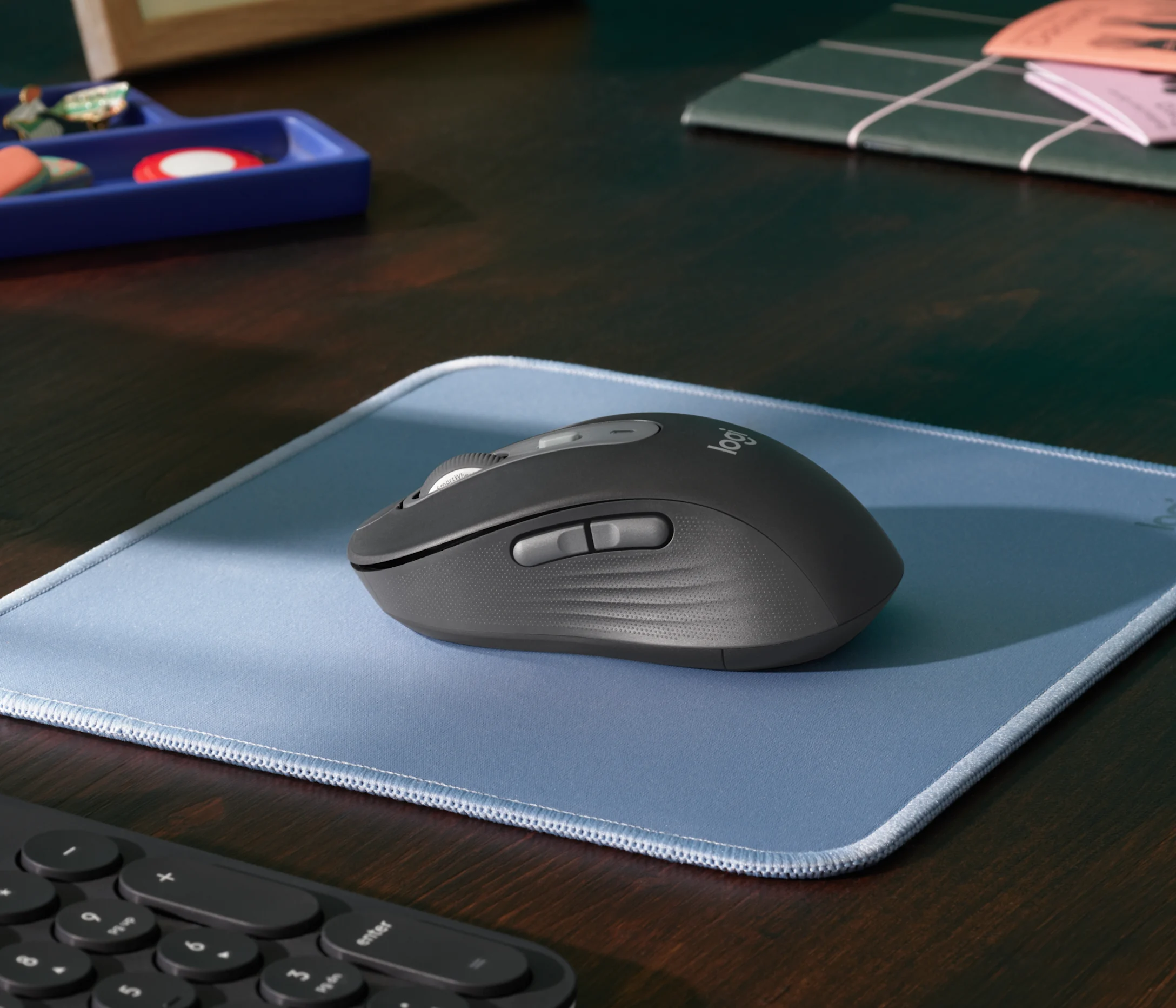 Une souris d'ordinateur sans fil grise sur un tapis de souris bleu posé sur un bureau en bois.